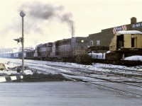 On a very overcast February afternoon, CP RS-10 8470 and RS-18 8732 have their work cut out for them as they pull an over tonnage train west on the Cartier Sub in downtown Sudbury, Ontario.  Out of sight is S-2 7090 shoving hard on the caboose to help keep the train moving.  The crane on the flat car beside the locomotives looks like it has had a pretty rough life.