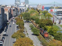 A CN transfer powered by CN 4129 & CN 7229 is exiting the Port of Montreal, with well cars up front and mixed freight out of sight further back. Paralleling the CN Wharf Spur here is a bike path and De la Commune Street.