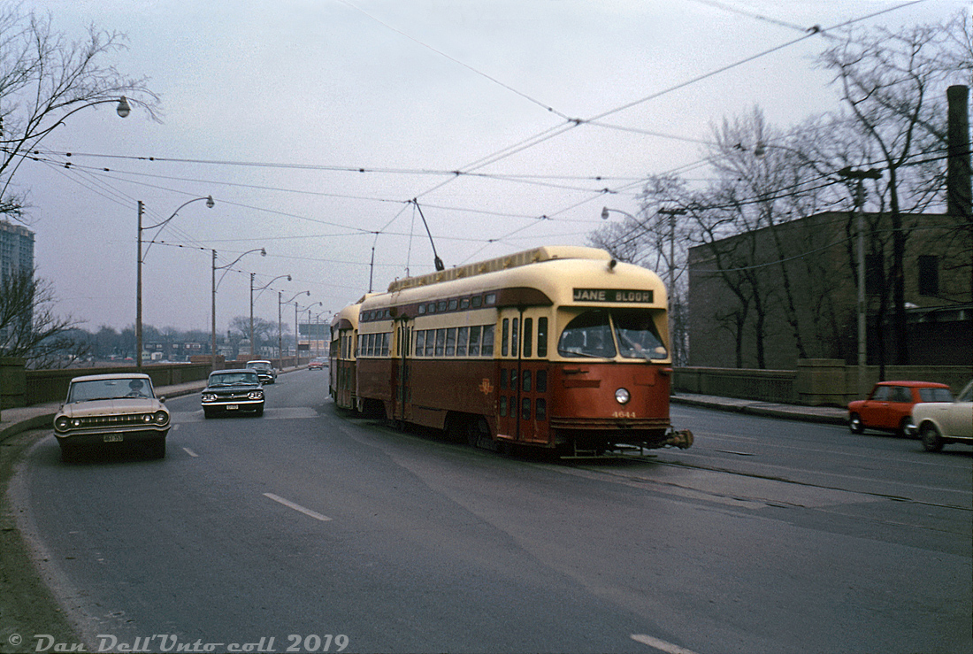 TTC PCC 4644 (an A11-class car originally built by Pullman in 1946 for Cleveland) operates in MU with a sister car on the busy Bloor route, heading westbound in evening traffic crossing the Bloor Viaduct (otherwise known as the Prince Edward Viaduct) near Castle Frank Road. Some of the TTC's PCC fleet (notably the 4400- and 4600-series cars) were outfitted with Multiple Unit couplers at either end for use as two-car trains on busy routes such as Bloor, Danforth, and Queen. Other cars had metal bumper strips installed in the opening where the coupler would go (and later, conventional water bumpers).The exact date of this shot is unknown, but going by the processing stamp of March 1966, this was likely taken around the end of the Bloor-Danforth streetcar service sometime in February 1966. The new subway line opened on February 26th and eliminated most of the busy Bloor and Danforth streetcar route, except for short "shuttle" runs at both ends of the line that were operated until further extensions opened in May 1968. Ironically enough, the Bloor Viaduct had been built in the 1910's with the forsight of a lower deck under the roadway for any future rapid transit lines, so the rails over the Bloor Viaduct were effectively replaced by rails under the roadway when the B-D line was built 50 years later in the early-mid 1960's.Original photographer unknown, Dan Dell'Unto collection slide.