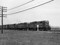 Two MLW RS-18 locomotives built 1960 or 59, with an RS-10 built 1955 between them, lead a train with 40 foot boxcars.<br>
Locos and cars in this image all wear the CN leaf scheme, the locos in olive green with yellow/gold accents.<br>
Several B-B road switchers of 1800 HP or less and a train of mostly boxcars seems to be typical of the era.<br>
Location mapped is approximate.
