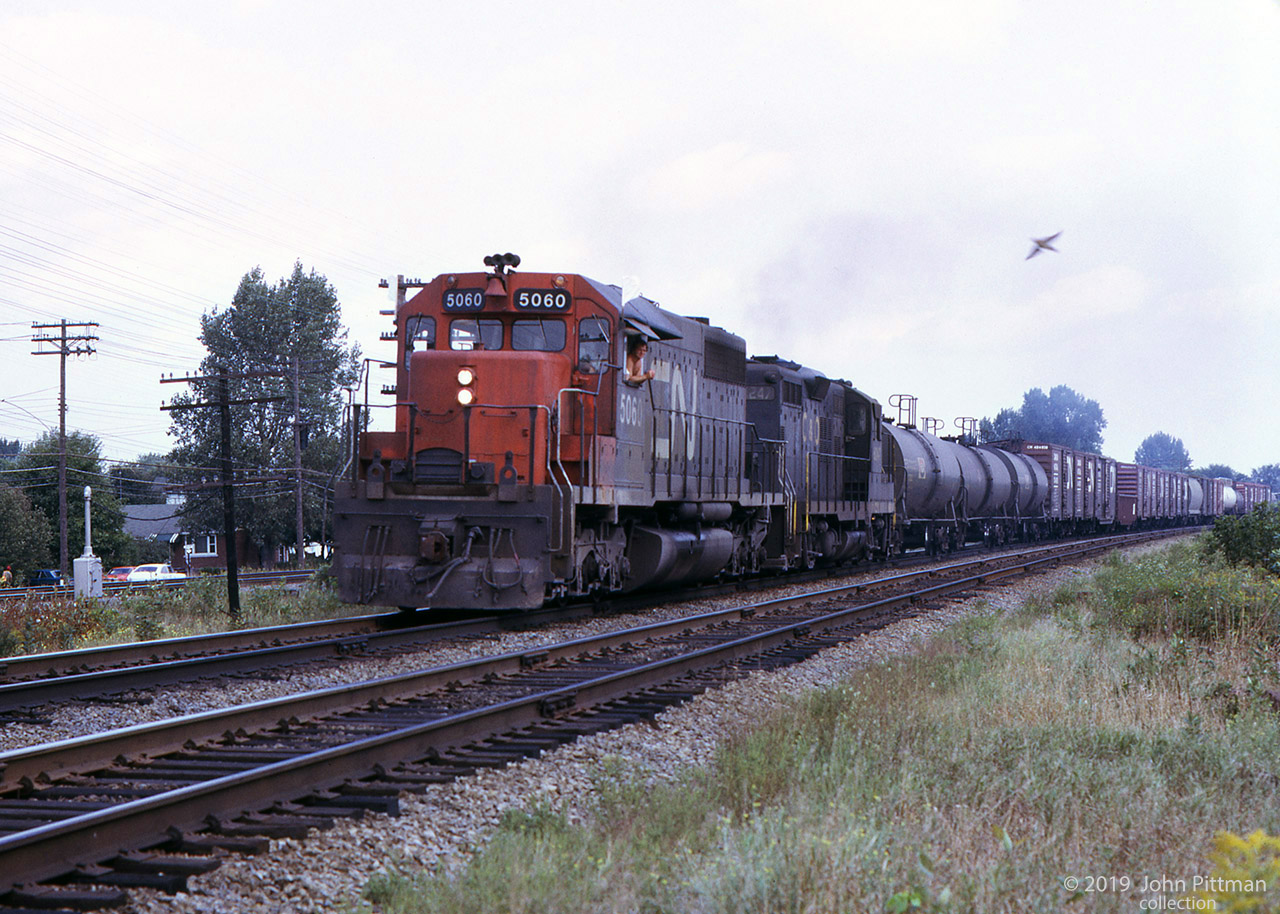 Westbound CN freight train at Pointe-Claire QC, powered by GMDD SD40 CN 5060 and EMD GP9 C&O 6247. 
From the crewman's posture, the train is either moving slowly or halted - the bird is much faster.
CN and CP main lines run parallel in the western part of Montreal Island, CP tracks can be seen on the north side.
Location mapped is approximate.