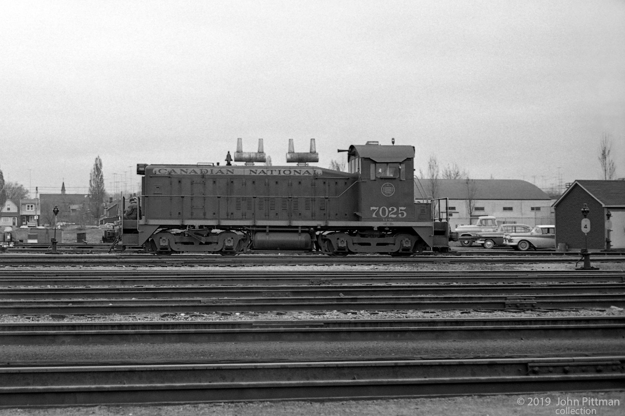 CN 7025 is a standard SW1200 switcher with AAR-A yard trucks, built by GMDD in September 1956. 
The walkway below 7025's radiator intake is clean enough to sit on, at least in overalls. 
CN predecessor Grand Trunk Railway built Danforth Yard - it no longer exists.
Vehicles of the era are at right; note the high television antennae above the homes in the background.
GO Transit Danforth Station near Main St has been mapped (approximate location).