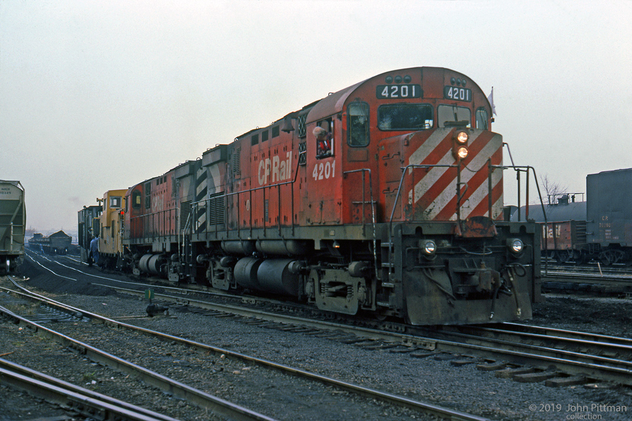 A pair of CP MLW C424's works in Aberdeen Yard with a TH&B Angus caboose and a (Jordan?) spreader/flanger.
Further back in the siding are side-dump cars loaded with dark-colour material to build up the ballast.
A fair amount of this material has already been dumped and spread. Some siding tracks look wavy. 
Within a couple of months CP would take full control of the TH&B, ending its separate existence.
Location mapped is approximate, assumes east end of yard.
