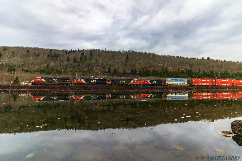 On a calm, cool Fall morning, train 120 crests the climb at Folly Mountain, seen here passing the still waters of Folly Lake, Nova Scotia.