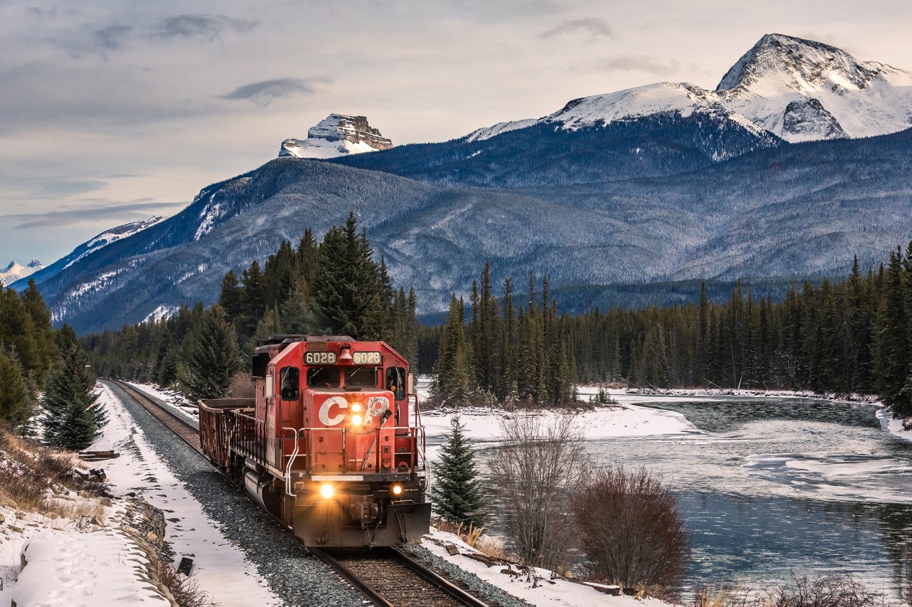 Behind the blue Rockies the sun is declining as a lone SD40-2 hustles along the banks of the Bow River with a single gondola for Eldon.