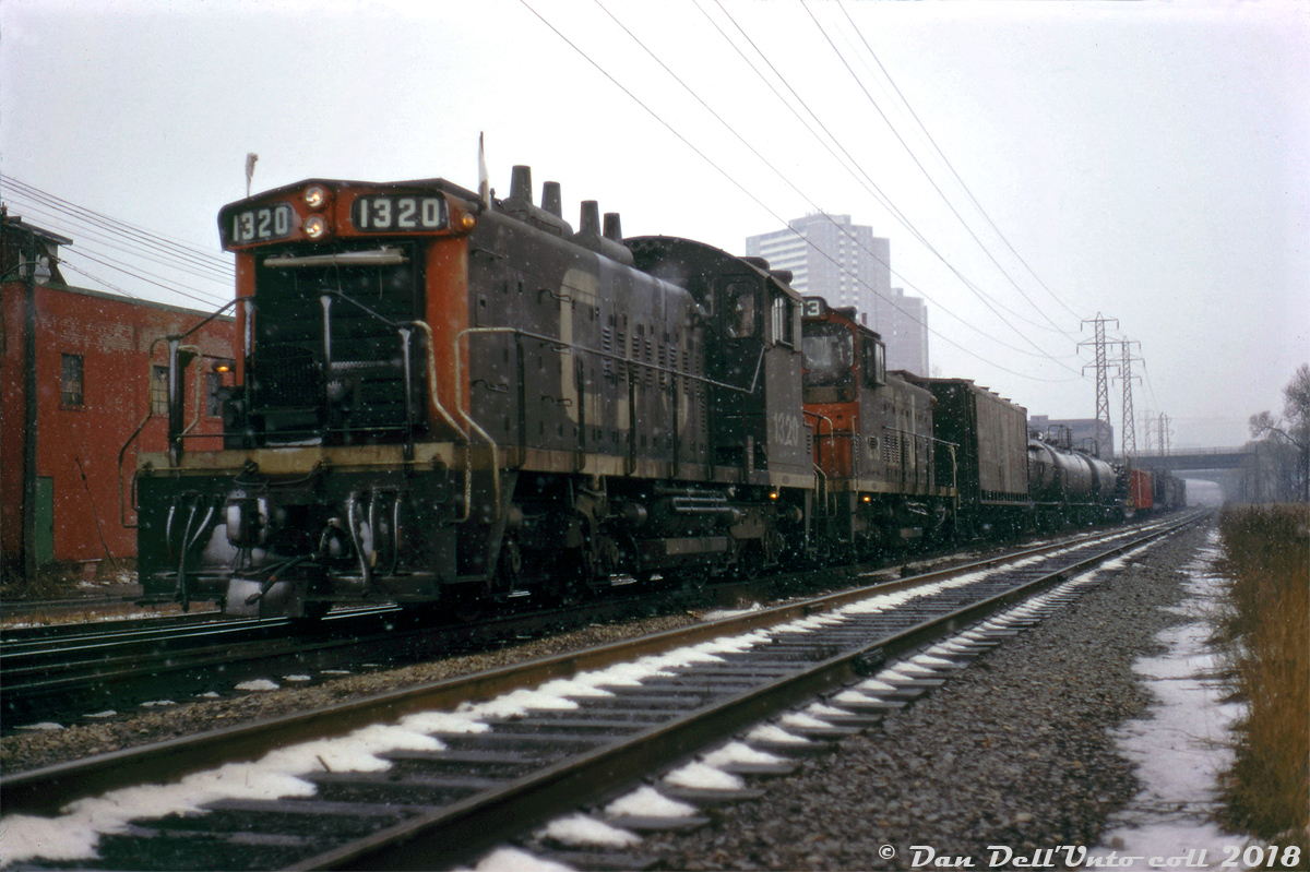 Heading southbound through the Don Valley in the snow, CN SW1200RS units 1320 and 1213 lead an extra freight down on the Bala Sub through "Don" (the interlocking at Queen Street bridge), stopped while awaiting the light to enter Toronto Terminals Railway territory (the downtown Toronto trackage around Union Station, presently the USRC). This could be a transfer freight from MacMillan Yard for either Don Yard, or possibly Mimico. Note the three tracks, the closest of which is CP's Don Branch (the Belleville Sub) from Leaside, then CN's Bala Sub mainline from Doncaster diamond, followed by CN's P500 service track.  This slide was part of an interesting series of photos taken by an unknown photographer, showing multiple meets between a southbound CP transfer down the Don Branch lead by RSD17 8921 "The Empress" (and caboose 438811), meeting a local freight headed by CN S2 8136 that was switching some of the industries around the Don/Cherry St. area on the service track, later followed by this southbound freight lead by 1320 & 1213 down the adjacent Bala Sub.  Original photographer unknown, Dan Dell'Unto collection slide