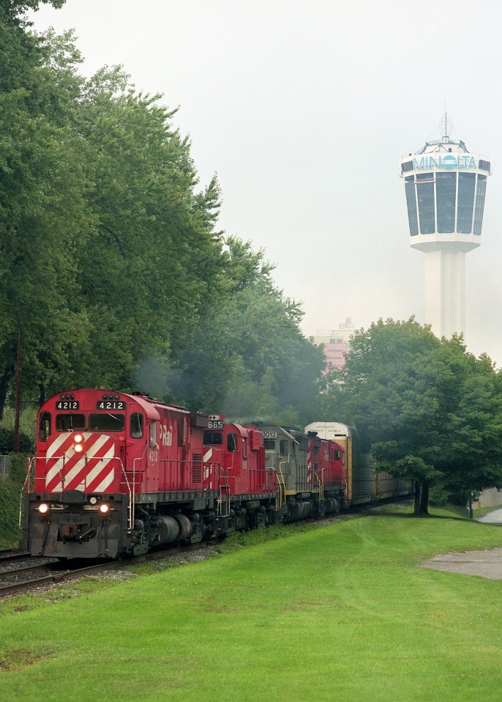 Watching for trains coming over the bridge from the USA and thru Niagara Falls back in the 1990s could be hazardous to your health. For one thing, you could get yelled at or run down if you were not careful. The tourist areas were murderous for auto traffic, as well as wayward visitors not knowing they are stepping into your attempted photo.
The ace-in-the-hole was to motor over to the South Siding Switch at the south end of town. Today, this location is good for the odd Chippawa industrial images, as that is all the traffic there was left once the track was torn up thru downtown around 2001.
Good quiet location to pull over and wait for a train was right here. In this view CP 4212, 1865, PNS 3013, and CP 4214 haul Toronto-bound traffic on a warm summer evening; which is when most trains seemed to make an appearance. Either that or after sunset.
Not many PNC (Precision National) units to be seen, but at this time power-short CP was grabbing just about every serviceable unit they could get their hands on. And hope they kept running.
Today, the tower in the background is pretty well buried in the forest of new highrise buildings, hotels, condos, what have you. And the expansion is still on-going. Council last week passed plans for a 72 floor building downtown. In tacky town Niagara Falls, it appears the sky is the limit.