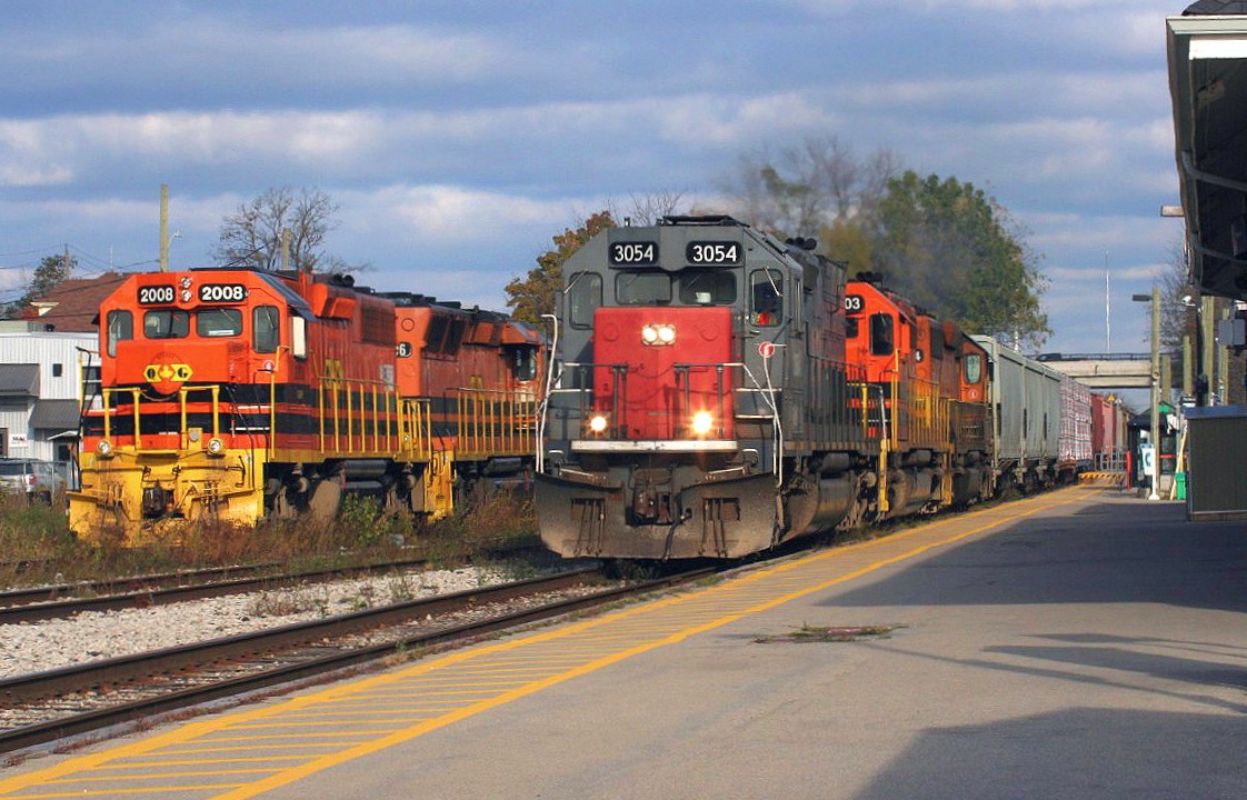 Goderich-Exeter Railway (GEXR) road train 431 with GEXR SD45T-2 3054, RLHH SD40-2 3403 and GEXR SD40-2 3394 are accelerating westbound by the Kitchener VIA Rail station. To the left, QGRY 2008 and SLR 3806 await their next assignment on 584 after having just returned from Guelph on train 580.