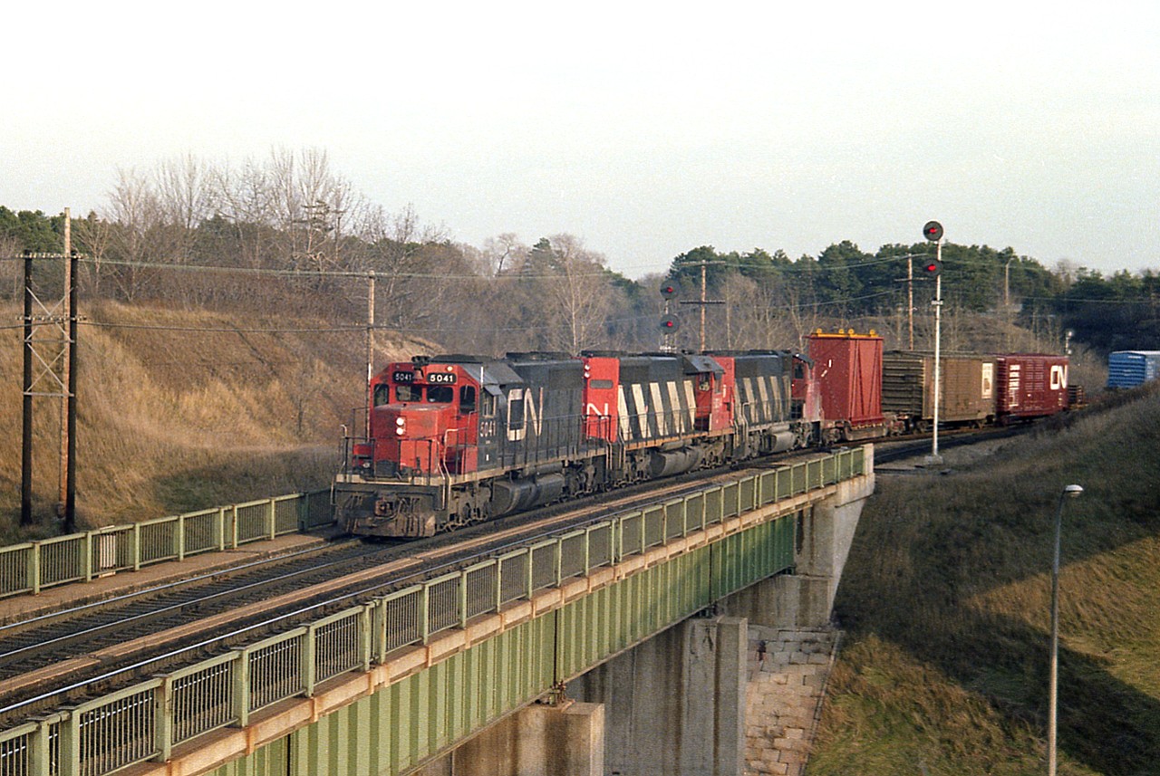 Most of us agree that very late fall thru early winter is often the most drabby time of the year for scenery. But diehards still go out hoping to see something that is interesting enough that the landscape really does not figure so much.
One such capture that left that impression on me is this photo. I guess because it is of an odd location compared to where I usually shot.
Westbound CN about to roll over the Highway 403 bridge as it rounds the bend at the old Hamilton West junction. Weak afternoon sun. Actually helps the overall scene. Closer to an evening 'sweet-light' than a 1430 hrs image.
CN 5041, 5034 and 9635 is the power. The straight SD-40 are off the roster, as are all in that series; and 9635 is now #8015 on the Rocky Mountaineer! (The two SDs were peddled off to BNSF.)