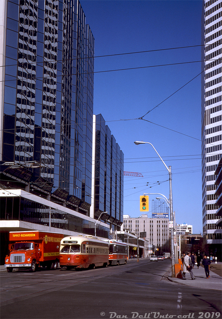 The 1980's were a transition era for the TTC's streetcar fleet: the introduction of new CLRV streetcars in the late 70's/early 80's displaced a lot of the aging PCC fleet, notably the remaining secondhand cars the TTC bought. Most of the A6-A8 class PCC's built new for the TTC (4300's, 4400's and 4500's) continued to soldier on side-by-side with the CLRV fleet, but the later arrival of the articulated ALRV's in the mid-late 80's culled most of the fleet. A group of the A8's were rebuilt as 4600-series A15's, and used for a few more years of service on the new Harbourfront LRT line into the 90's.

Here, TTC PCC 4473 (an A7-class car built in 1949) and CLRV 4059 (a new CLRV built in 1980) wait on Dundas Street for the light at Bay Street, next to a Ford L-series "Louisville" truck operated by Tippet-Richardson, a popular moving company around the city at the time. The new Atrium on Bay (built early 80's) towers on the left, and the Eaton Centre's north tower (that contained Eaton's head offices) as well as their parking garage line the south side of Dundas. In the background is Yonge Street, and Ryerson's Victoria Building (seen here).

Original photographer unknown, Dan Dell'Unto collection slide.