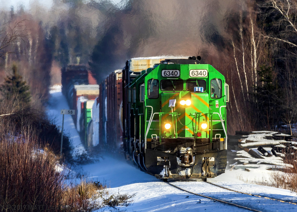 Maine Northern 6340, ex Southern Pacific, now in NBSR Green, leads westbound train 907 as they approach Cork, New Brunswick, negotiating the ups and downs of the McAdam Sub.
