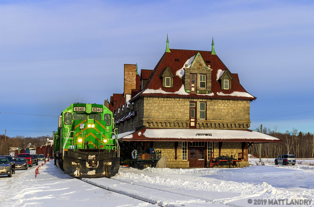 MNR 6340 leads NBSR train 907, as they pass the famous railway station in McAdam, New Brunswick, coming in for a crew change.