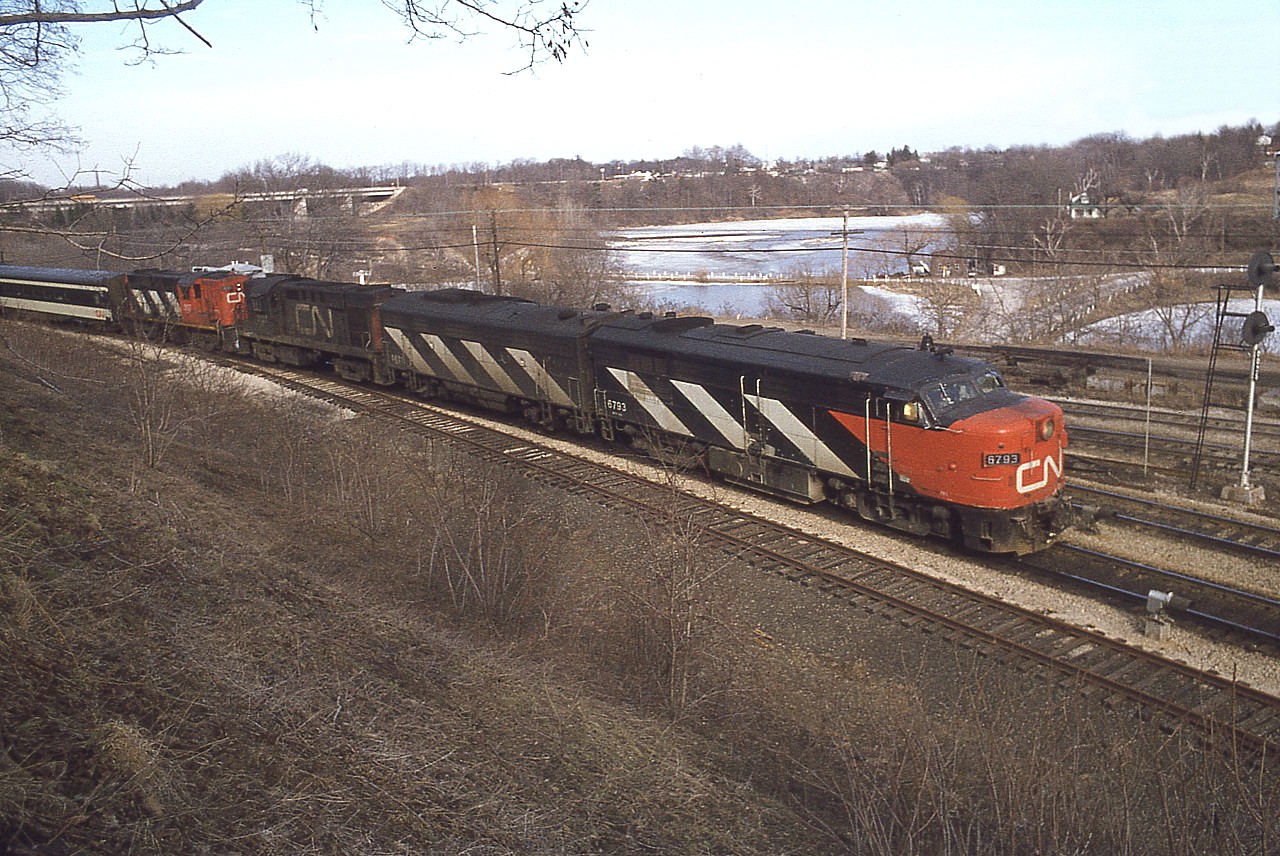 Nothing to indicate VIA is going to be that big Canadian passenger train outfit just yet. In the days just before the formation of VIA the power consists on many of the premier passenger trains was quite interesting. And with the gradual transition to the new VIA colours in the immediate years to follow, it remained so. I got out trackside as often as I could. Thats my explanation for so many lousy light photos. :o)
This wide-angle image off the Botanical Gardens hillside shows a typical #75 of the day, no doubt a weekend train, as they were quite heavy, but I forgot to mark the exact date on the slide. CN 6793, 6627, 3121 and 3107 is the power. Of interest is the 6793 is now on the Grand Canyon Railway down in Arizona.