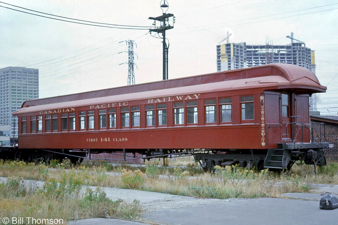 Restored CP "First Class" coach 141, dating from the early 1900's, is seen at John Street coachyard in downtown Toronto, brought out of storage for Railway Days in October of 1973. In the background, you can see the Toronto Star's office tower at 1 Yonge Street, and another high-rise tower under construction along the harbourfront.

During the planning of CBC's "The National Dream" series (with Canadian host Pierre Berton) in the early 1970's, CP was looking for old equipment suitable for use in the series of episodes portraying the creation and building of the railway. This car was originally built by CP's Angus Shops in July 1907 as suburban coach 141, and at the time was one of only three such cars left, assigned to OCS / Maintenance of Way duties on the DAR and numbered 411585. Originally a sister car was the one picked, but after it was damaged in transit, car 411585 and the remaining other car (for parts) were shipped to Weston Shops in Winnipeg for restoration in 1973. 411585 was given back its original number 141, and decorated to represent an earlier era for filming the 1870/80's-ish footage. The car, along with famed CPR 4-4-0 steamer 136 were both featured prominently many scenes of The National Dream. CP later donated 141 in 1980 to the Calgary Heritage Park, where it currently resides on display and restored to its original varnished wood exterior.