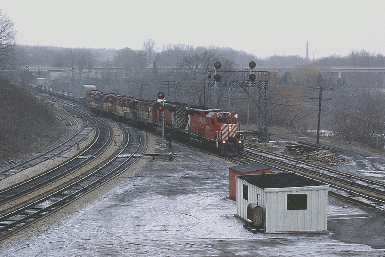 You could say a TH&B train with CP power on CN track.
What a crummy day. I remember this Sunday rather well. It was early spring (yep!) and it was totally miserable but a lot of guys were out as the 'spring fever' was in the air. Until today. Damp wet snow took away the sharpness we would have otherwise had in the days' photos.
Having nothing else in mind, I hung in for the Starlite after almost everyone else had left; and it rolled along just before the dinner hour with 7 units. Can't find my notes. Only notice lead unit is CP 5725 and there is what looks like an CP RS-18 on the end behind the 4 horses of the TH&B.
Of note in the extreme background is the chimney of the old Burlington Brick plant, long demolished.
This image, BTW, was shot with Sakuracolor print film using a Pentax K-1000.