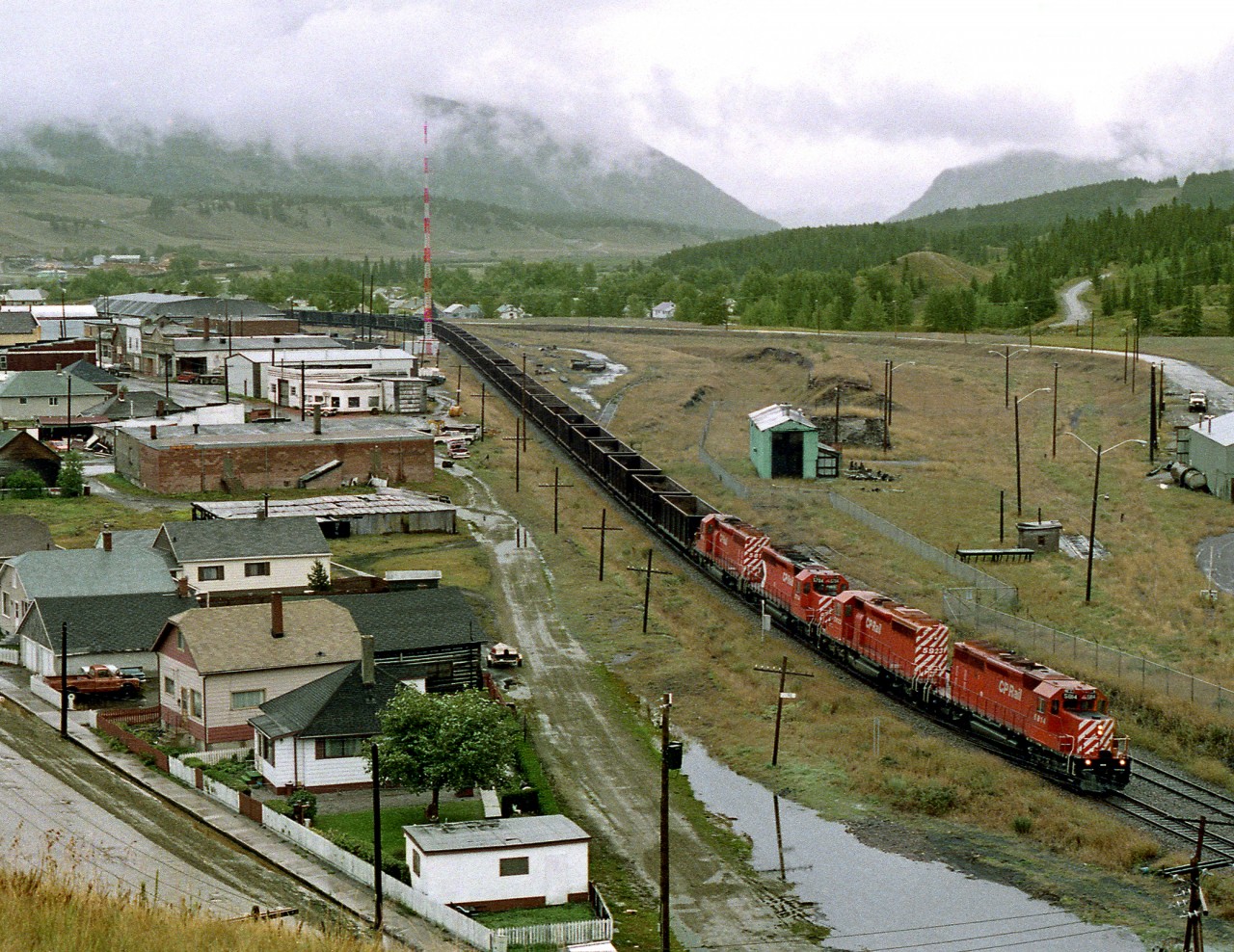 Coal empties from East Chicago to Line Creek, in B.C.'s Elk Valley, pass the old coal mining town of Coleman on the east slope of Rockies. The remains of the old mine tipple, yard and coking ovens lie to the right of the train