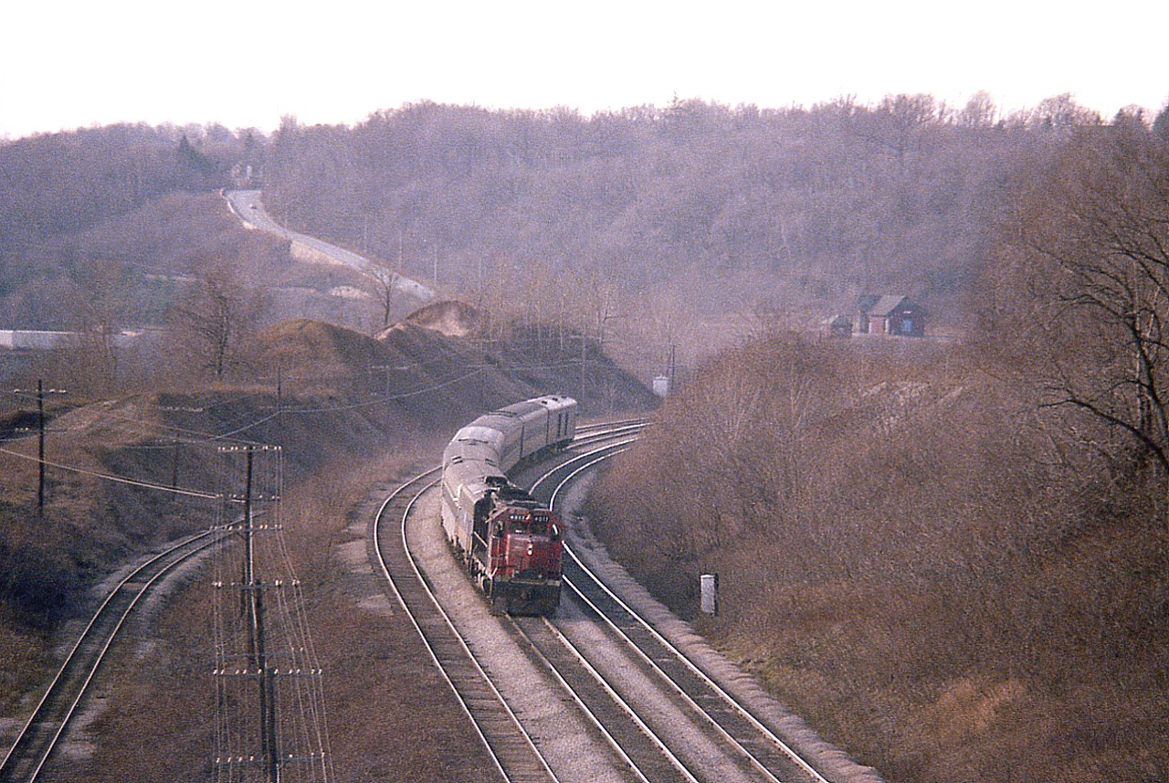 Another one of those dismal sort of days in early December, with a hint of low sunshine, but what hurt was being let down by some inferior film this time around. It must have been that old Sakuracolor, an imitation po'boys Kodak that I should have never bought.  Very grainy.
This view is from the old Canada Crushed Stone conveyor that used to straddle the tracks carrying stone from the north hill side over to the stockpiles at Steetleys area down below the CN main. In this view foreground, the two right tracks are the main, the left is CN siding, well used, and down in the "gully" is the line off the CN that not only served Steetleys and their dolomite business, it also connected to the TH&B which accessed via the line that came thru Dundas!
Top right; old Dundas station and section house across the tracks. Hwy 8 coming down the hill on the left. A lot to see in this view.
Power on "VIA" #72 is CN 4017 and VIA 6621.
The area mentioned 'down below' the track is now a housing complex.