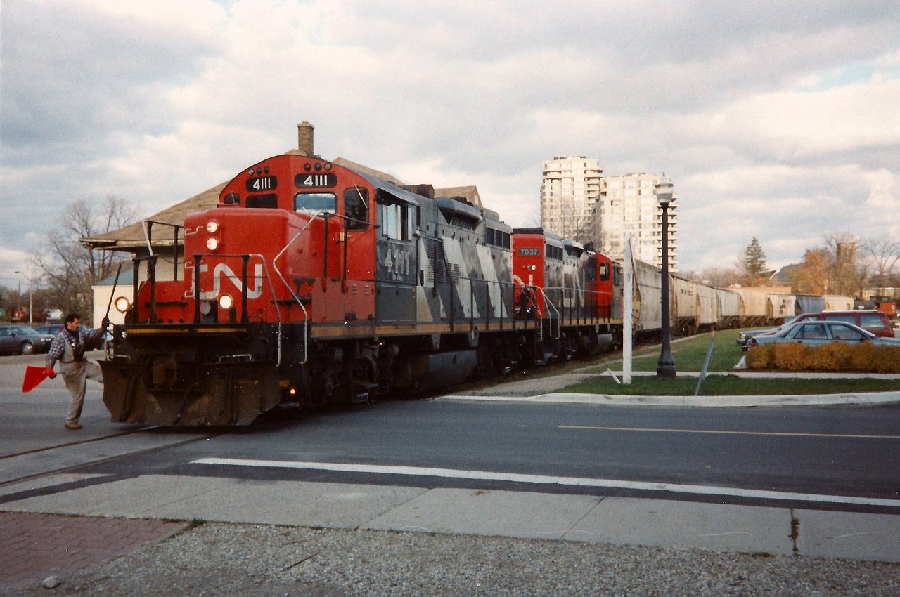 The CN 15:30 Kitchener Job has a lengthy train destined for Elmira as it crosses Regina Street in Uptown Waterloo with GP9RM's 4111 and 7037. At the time, it wasn't common for this assignment to operate with two units, as most jobs out of Kitchener usually just ran with one during the mid-1990's. However, due to the 8 hoppers for Nutrite in Elmira, the crew opted to use two as they also had a tanker for Sulco as well as caboose #79905. Most trains on the spur weren't this lengthy at the time, however seasonal demands in the spring and fall would dictate otherwise on occasion.