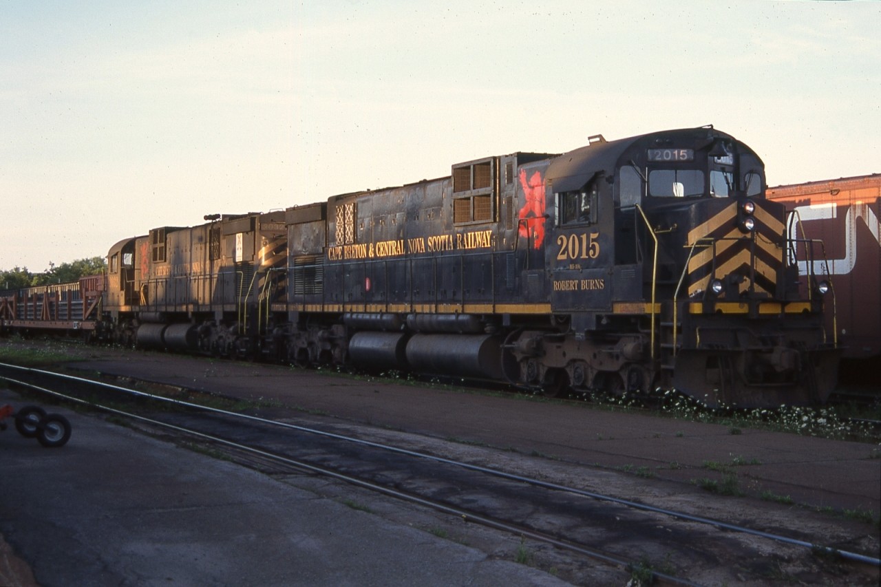 Cape Breton & Central Nova Scotia C-630M Nos. 2015 (ROBERT BURNS) and 2032 (LORD BYRON) are shown on a late summer Saturday evening. Constructed by Montreal Locomotive Works (MLW) for Canadian National in 1968, both would be acquired for the start up of the short line enterprise in October of 1993. While No. 2015 would be retired in 1996, No. 2032 would toil away for a decade along the east coast of Canada prior to being sold for scrap in 2003. Note the CN company service flat car with a load of rail from Sydney Steel Corporation.