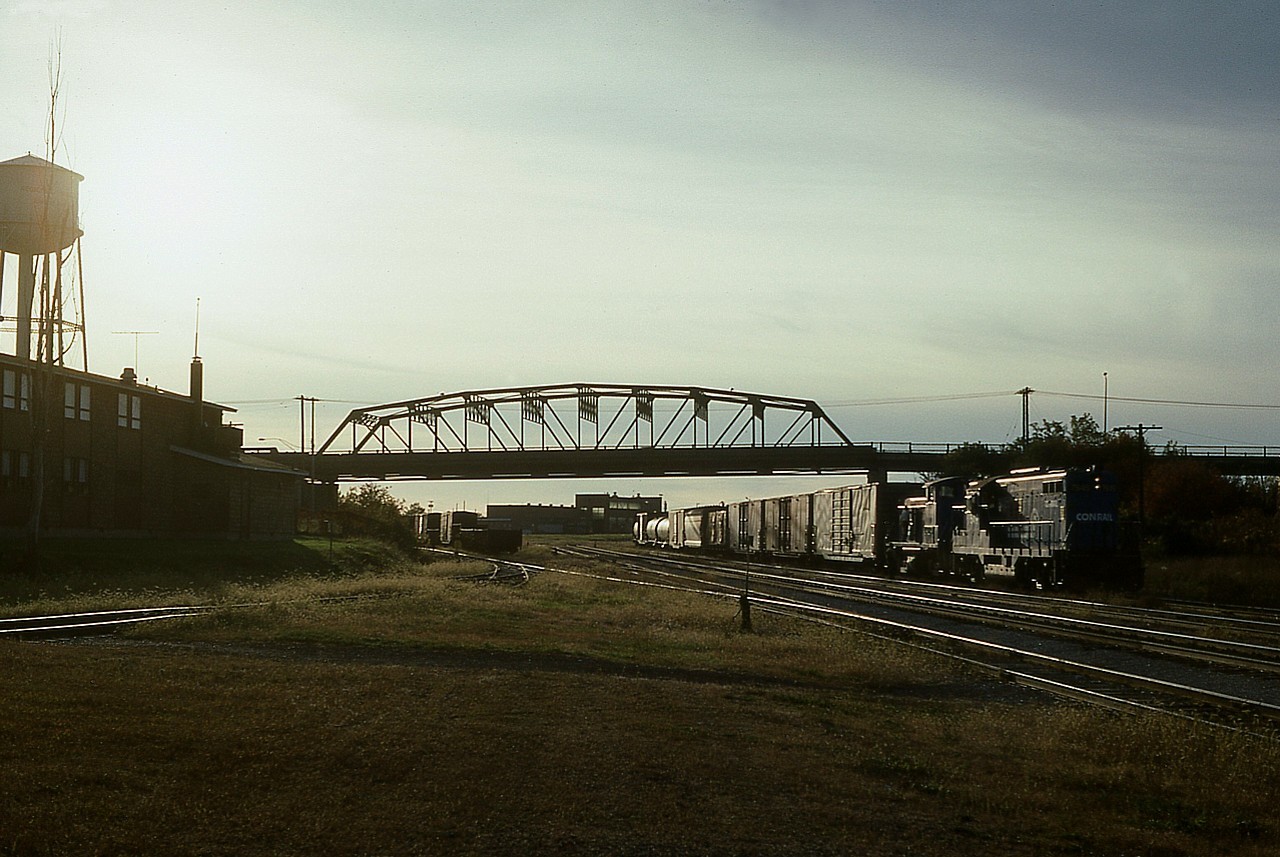 Some days I just did not want to go home.  Had a great day at Fort Erie.  Those who are familiar with shooting down that way know the havoc of the sun angle. It always seems to be in the wrong position........unless there is something coming over from the states.
I didn't think much of this effort, as it is an image shot via slide and I wasn't going to see the results for a week or two. Not instant stuff like today's digital age. I didn't even bother to log the numbers. (7549 & a 95xx)
Looking back now 35 years this shot has some historical interest to it.  Sure, Conrail is history, but so is the bridge as of late, the water tower and the CN crew hostel on the left. I am not sure when it came down, but the base is still there because I park on it watching for trains coming off the bridge. As for the water tower, I was looking at some pics one day and....hey!...what happened to the water tower?  I guess I should have paid more attention to details..................