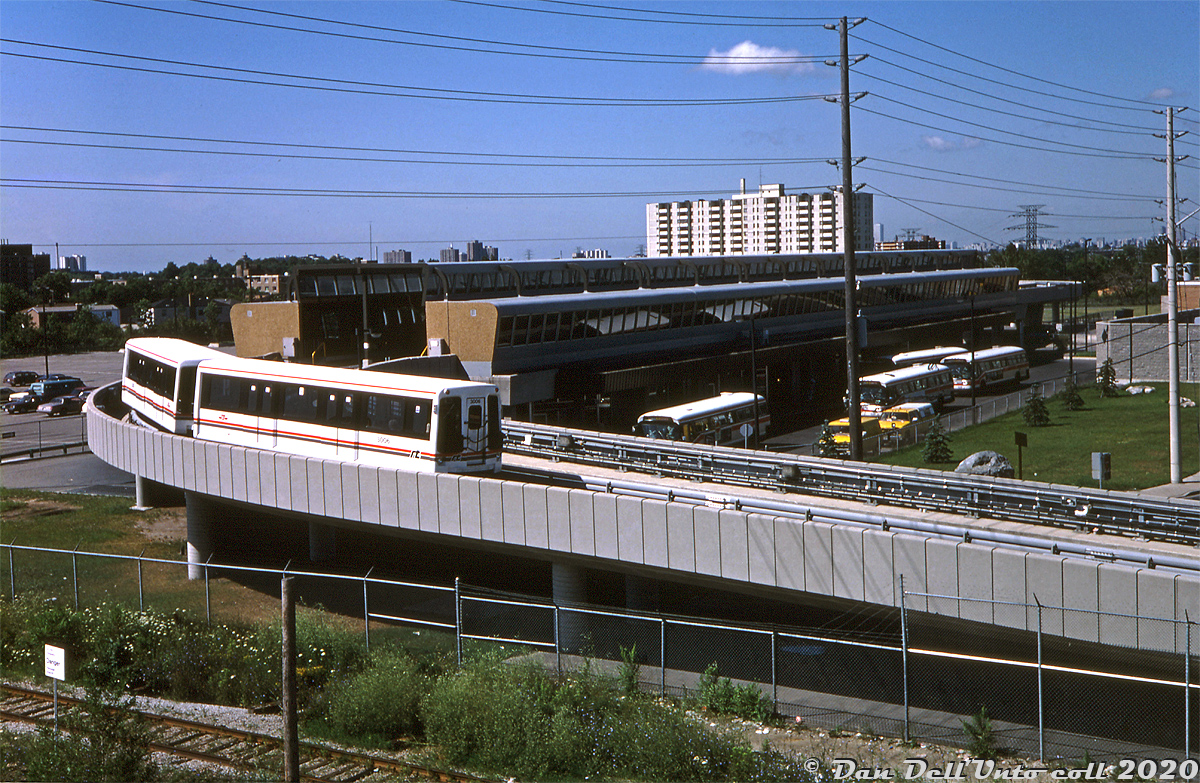 Toronto Transit Commission ICTS cars 3006 and 3007 are seen outside Kennedy Station during the two-month Scarborough Rapid Transit (SRT) line's free ride period for the public (over a small portion of the line), still a few months away from full completion and opening for revenue service in March 1985. The joint Kennedy subway/SRT station featured the SRT platforms on the upper level, the bus terminal concourse at ground level, and the subway platforms for the easternmost end of the Bloor-Danforth line below. A school of the TTC's classic GMC "fishbowl" buses populate the bus terminal. In the foreground is the CN's Uxbridge Sub that runs alongside part of the SRT line.

Reminiscent of an 80's zoo monorail, the Scarborough RT was the result of 1970's Scarborough wanting a link to the rest of Toronto's subway network. A lack of density along the route (lots of low-density residential and industrial lands) didn't warrant a costly full subway line extension, so the TTC was initially building it as a grade-separated LRT to use the new CLRV streetcars (operating alone or in multiple/MU) to service it. Due to political pressure by the Ontario government of the day, they ended up changing plans and building the line to run the government's expermental Intermediate Capacity Transit System (ICTS) instead, essentially a halfway transit solution between a streetcar and a subway.

Much to the government's disappointment, their ICTS system never caught on outside of a few transit agencies (notably Vancouver and Detroit) and decades later, the TTC's Scarborough RT system is an orphan on the system that has reached the end of its lifespan. The equipment is old and obsolete, and can't be easily replaced by new off-the-shelf design cars due to restrictions on the line, nor can the line easily be upgraded to handle modern equipment or even a subway itself.

The SRT had been green-lit in the 2000's to be replaced with a fully funded LRT system, until the election of Rob Ford - who cancelled the LRT in favour of his promise of building Scarborough a subway extension of their own instead. Years of political squabbles followed over the costs involved of replacing it with an LRT or subway, subsequent councils changing their minds a few times, and later how much of the proposed subway extension should (or could) be built. In the meantime, the TTC has manged to kept the SRT running, and the residents of Scarborough keep waiting for their "someday, someway" subway promise.

Original photographer unknown, Dan Dell'Unto collection slide.