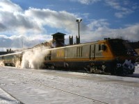 VIA LRC 6911 leads a steam-heated passenger consist of blue and yellow cars on a chilly day in January 1990, stopped at the station in Guelph. Steam generator cars were necessary when running older equipment with LRC or F40PH locomotives, as they were delivered with HEP generators for modern equipment, rather than steam generators that the older cars required.