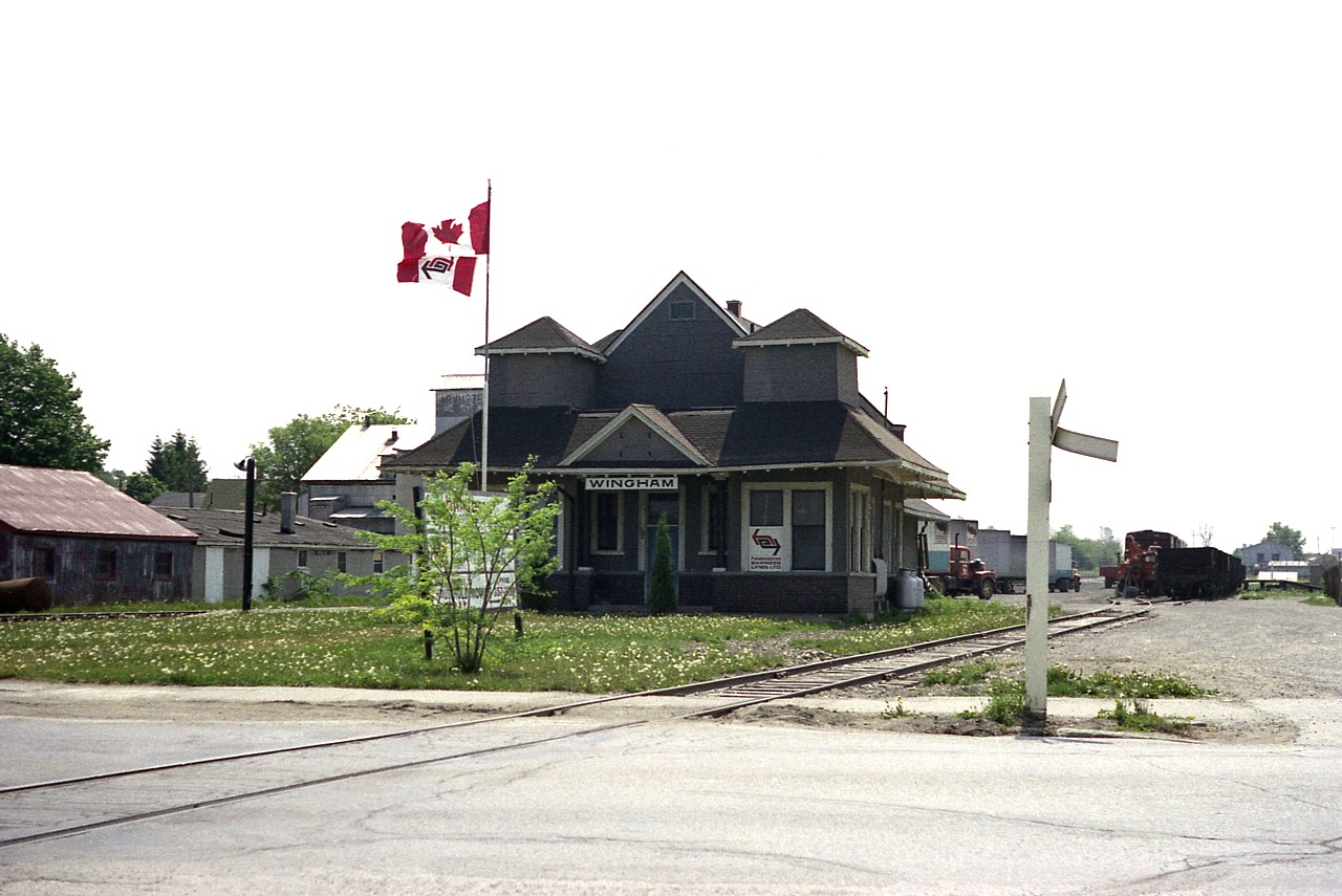 The CN station at Wingham still stands, and lovingly restored. It even has a steel roof. Back in the day when I shot this photo the former station was mostly occupied by the offices of Harkema Expressway, a trucking company that I am told took over Walden Brothers.  The offices were here only briefly, generally the company based out of London and Brampton.
In this view you see the company banner flying below the Canadian flag; you can see a few cabs and quite a few trailers out back as well as some rolling stock on the CN trackage.
It is a welcome sight to see such an unusual structure soldier on, looking better today than it ever did.