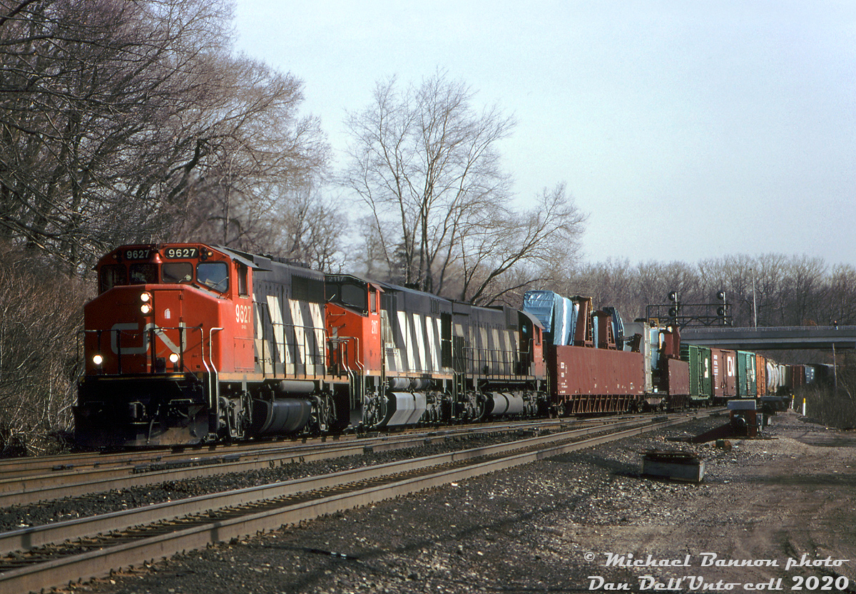 A westbound CN freight lead by GP40-2LW 9627, HR616 2117, and an M636 that appears to be 2309 head through the plant at Bayview Junction, ready to begin the climb up the Dundas Sub. Trailing the power on the head end are a pair of UP wing cars carrying aircraft wing assemblies bound for the US, enroute from the McDonnell Douglas plant in Malton ("MDCan") along CN's Weston Subdivision (which was formerly the famed A.V. Roe plant, home of the Avro Arrow).

Douglas Aircraft (later McDonnell-Douglas) purchased the Malton plant from de Havilland in the mid-60's and set up its branch plant operation there to make wing assemblies and other components for DC-9's. The DC-9 wing assemblies were transported on flatcars in pairs, forwarded to the MD plant in Long Beach, California for final assembly. When production of the DC-10 started up in the late 60's, specially-built "wing cars" were built by Maxson to handle the larger DC-10 and later MD-11 wing assemblies. They were essentially 88' long cushion-underframe gondolas outfitted for transporting the wings. Douglas Aircraft owned six of their own (DCCX 1001-1006), that were later joined by a group from Union Pacific (UP 229580-229587). Because the wing assemblies were so long, UP spacer flatcars were used in the middle of two wing cars to account for the wing overhang from each, and were usually handled on the head end of freights. From a bit of research, routing of the wing loads was from Malton via CN to GTW at Port Huron, who interchanged them at Blue Island (Chicago) to the Rock Island, who forwarded them to UP at Council Bluffs for final delivery to the Long Beach plant.

The old Malton plant operated for decades under McDonnell Douglas, was taken over by Boeing in 1997, and finally closed in 2005. The site was demolished in short order, and presently remains vacant. The big wing cars are also gone from the rails.

Michael Bannon photo, Dan Dell'Unto collection.