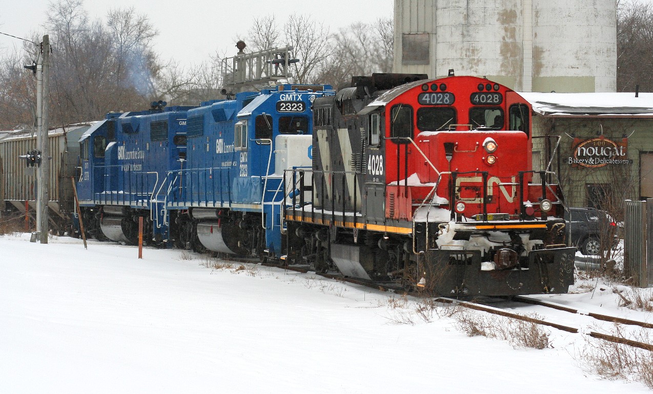 CN train L568 with 4028, GMTX 2323 and GMTX 2279 crosses Queen Street in Kitchener on the Huron Park Spur with hoppers for the interchange with Canadian Pacific during a frigid snowy afternoon.