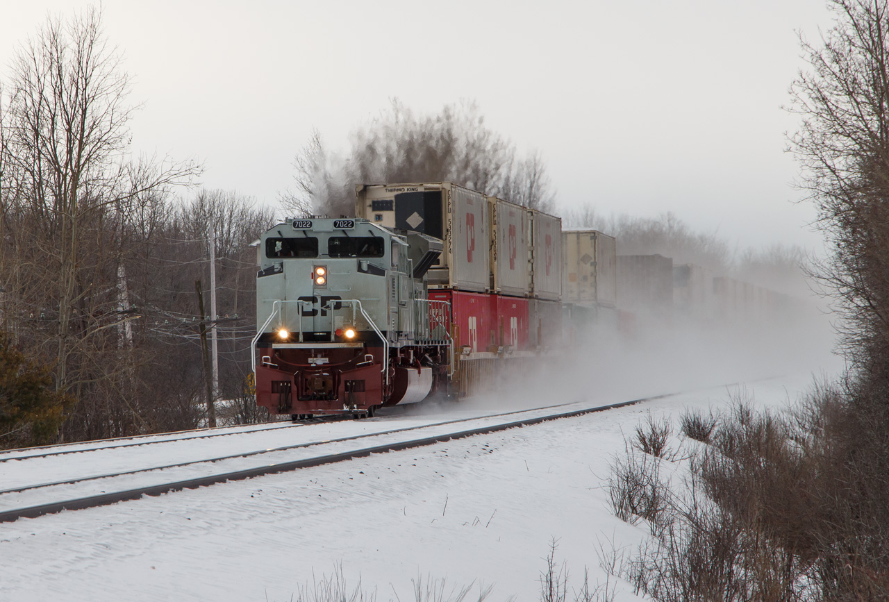 After setting off a defective car, eastbound CP freight #142 departed Smiths Falls at 1430 hrs on Sunday, February 9, 2020. From where I was standing on McCrea Road, seven miles away, the sound of the train throttling up echoed like thunder.

The train is led by "HMCS" CP 7022, assisted by mid-train DPU 8723 and rear DPU 8548. The three units had 142 up to the 50 mph track speed when it hit mile 116 at 1437 hrs. The grey of the lead unit and the vortex of snow enveloping the train are great camouflage for the gloomy overcast day, typical of winter in Eastern Ontario.

Scenes like this will change soon. The Winchester Subdivision is currently directional double track with OCS/ABS, but it is slated to be converted to single track CTC. New "Darth Vader" shrouded LED signals are being positioned beside some of the classic ABS searchlights, and track removal is likely to start in May.