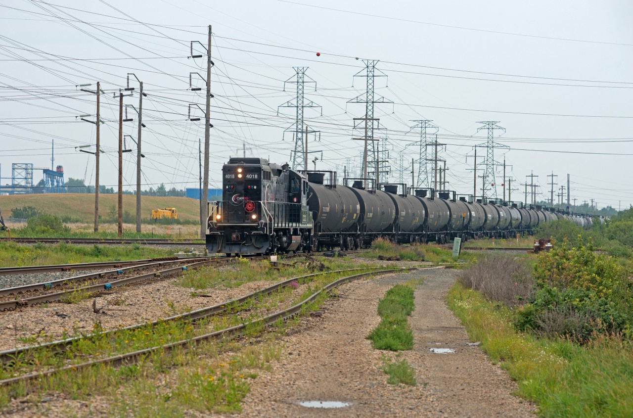 Exercising trackage rights on the CN Camrose Sub, Cando 4018 pounds across the diamond with the CP Scotford Sub at East Edmonton Interlocking. In the background one can see the seldom used (if ever) Genset switcher at the Kinder Morgan terminal and an exCN PSC Caboose that is/was used at a safety training facility.