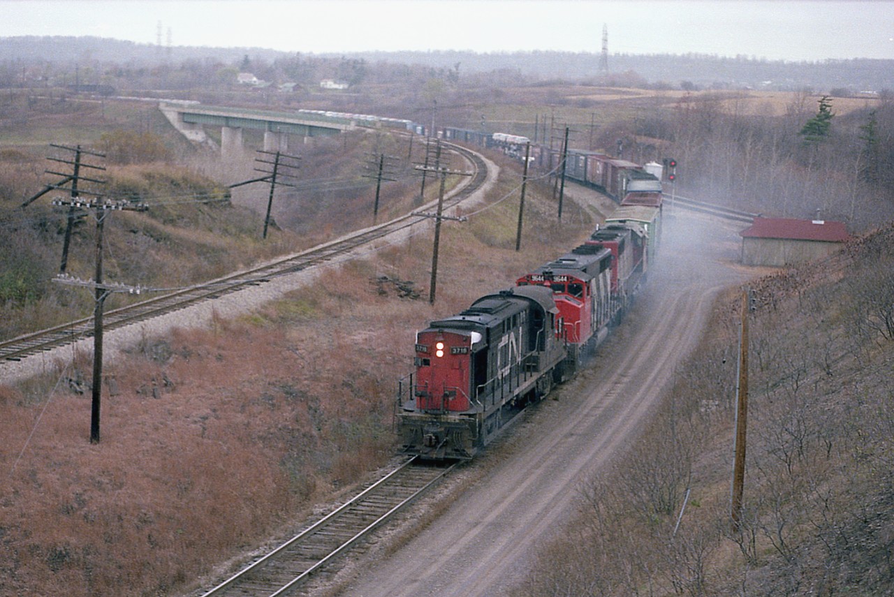 This, the day after the infamous Mississauga wreck, a CN RS-18, complete with 'extra flags' is seen coming off the CN Dundas Sub, en route for Hamilton.
I thought it rather unusual for this old MLW 3718 to be leading, trailing units GP40W 9644 and SD40 5068 would make more likely leaders, I suppose; but I enjoyed the opportunity to record this.
For those viewers out of the Ontario area, that is the CP Hamilton Sub line from the GALT sub on the left.