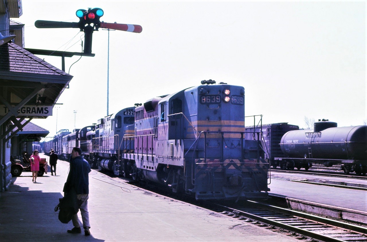 A westbound Canadian Pacific freight picks up orders on the move as it passes the Sudbury, Ontario station.  Note the train order hoop taking a bounce beside the lead unit.  The operator with the hoop and orders for the tail end is barely visible behind the guy who walked in front of me at the most inopportune time!  Power for the train is CP classic for the time period:  8639-4221-84xx-44xx-4069.