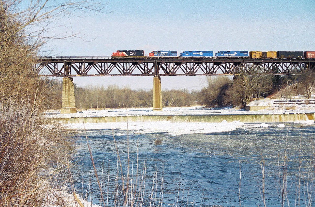 CN 391 crosses the Grand River bridge in Paris, Ontario on the Dundas Subdivision with a colourful consist. The unit’s included 6027, GT 5809, Conrail’s 6660 and 6751. Conrail SD45-2 6660 was on lease to power-short CN while SD50 6751 was working-off horsepower hours owed to CN at the time.