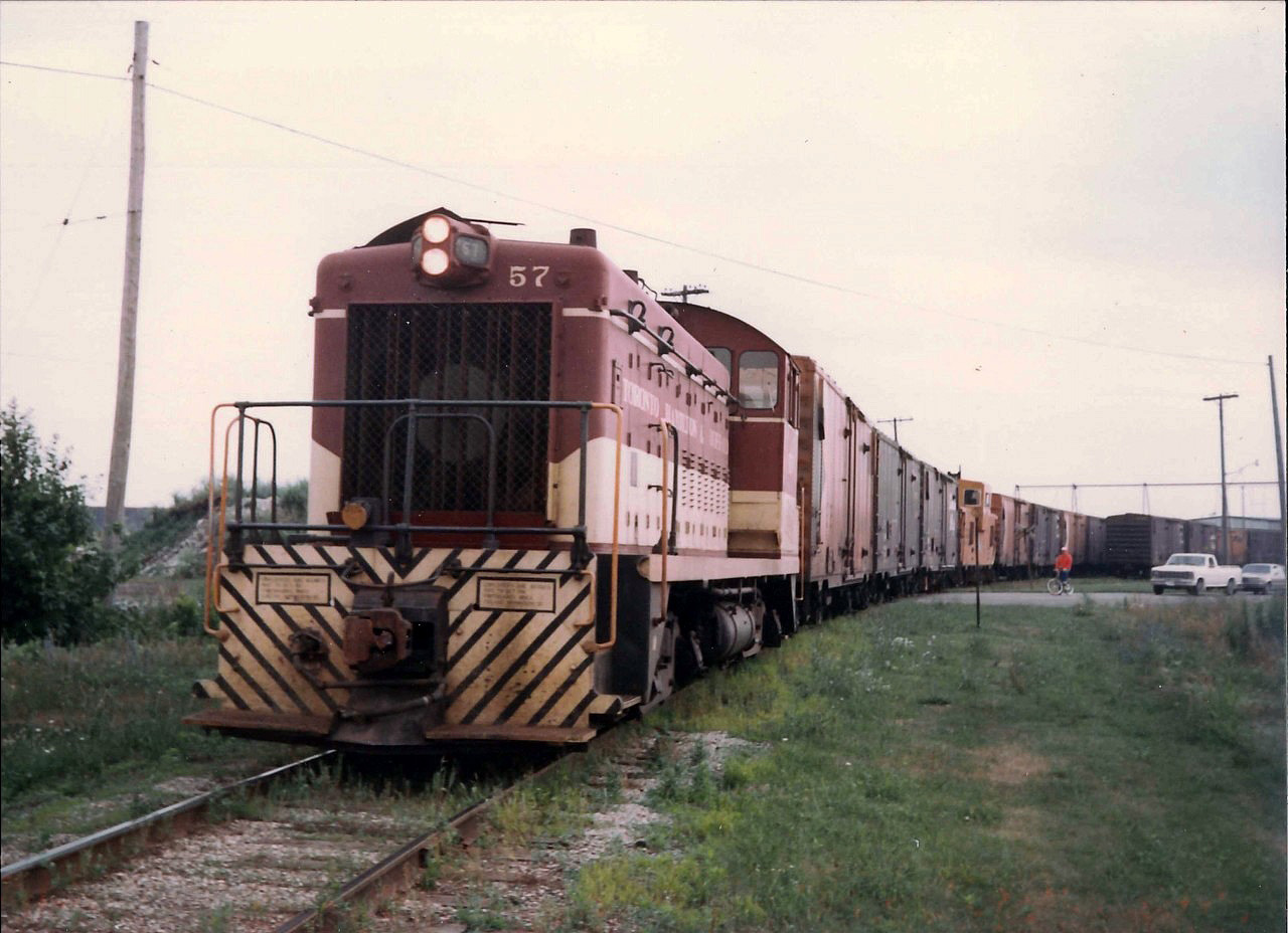 TH&B locomotive #57 is on boxcar switching duties at Maple Leaf Mills.  The once so common boxcars that filled the Port Colborne railyards would disappear completely within a few years.  The switching is holding up traffic at the King Street crossing. TH&B Van 83 is in the mix.