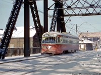 In another shot of the <a href=http://www.railpictures.ca/?attachment_id=38487><b>Bathurst Street bridge reconstruction work</b></a> in 1963-1964, TTC PCC 4393 (A6-class, built 1947-48) heads southbound on Bathurst Street south of Front, operating on temporary track laid on the west side of the bridge for southbound streetcars (the actual southbound track in the foreground was being used for northbound streetcars, while the two right lanes were closed and being redone). Note the relatively undisturbed snow on the bridge, as it was only open for streetcars and closed to regular automobile traffic.
<br><br>
The property to the northwest of the bridge behind the streetcar, once home to the Consumers Gas Company (one of their old coal gas manufacturing facilities, that had two very large gasometer tanks on site), was now home of the Kaufman Metal Company and the Toronto Refiners & Smelters Co. Visible in the distance is the Laura Secord candies building around Wellington. A keen eye would pick out something out of place here: a set of railway crossbucks. Those were for a industrial spur that lead across Bathurst Street (and the streetcar tracks at-grade via diamonds) to get to the Bathurst Tool building on the east side of Bathurst north of Front. As far as I can tell, this spur fell out of use sometime in the 1950's and was removed in the early-mid 60's, although I haven't found any decent shots of streetcars crossing it. For a 1947 aerial showing the crossing, click <a href=http://jpeg2000.eloquent-systems.com/toronto.html?image=ser12/s0012_fl1947_it0022b.jp2><b>here (check near the middle of the image)</b></a>.
<br><br>
<i>Photographer unknown, Dan Dell'Unto collection slide.</i>