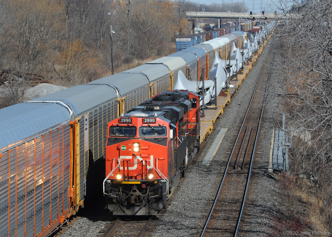 CN 319 is a unit train of windmill blades, westbound on Oakville Sub track 2 passing CN Aldershot Yard.
319's head end has just crossed Grindstone Creek bridge. CN train 422 on track 1 will proceed east shortly.
Another railfan told me he heard the axle count was 300. IF we got the axle count and math correct:
Deduct 12 loco axles leaves 288 flatcar axles, divided by 4 equals 72 flatcars. 
Each pair of blades occupies 3 flatcars, making 48 blades on the train.
It worked out well that my wife finished her shopping at the big blue and yellow store near Aldershot East around the time I learned this train was on the Halton Sub, heading towards us.