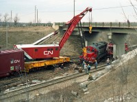 GP9rm mother unit CN 7263 will have its front lifted by Toronto Auxiliary crane CN 50008 to get it back on the rails.<br> The paint on CN 7263 is clean and glossy, so it's not long since its 1990 remanufacture.<br><br>
CN 7263 had been in a collision with GP38-2 hump switching unit CN 7508 which appeared to have got the worst of it, including having all its right side hood access doors torn off. Both units returned to service after repairs.<br><br>
According to my 1990 Trackside Guide, CN 50008 was a 250 ton capacity Bucyrus-Erie built in 1946.<br> 
Note the outriggers extended from the crane base and woodblock piles beneath to counter tipping forces.<br><br>
The bridge carries Rutherford Road over Macmillan Yard hump pullback tracks.<br>
Alan recalls taking these pictures in 1991. Foliage colour and some residual snow suggest March.