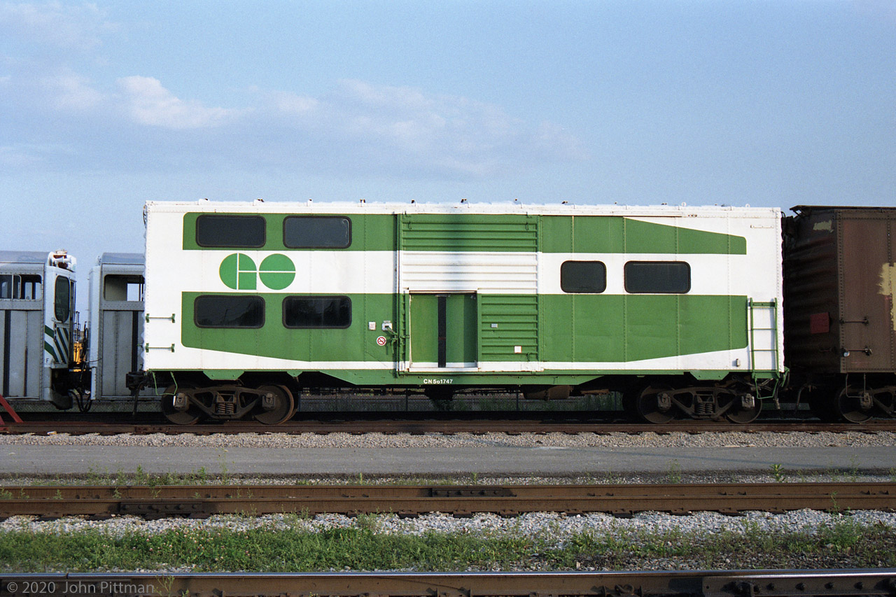 This unusual conversion of a 40 foot boxcar was seen in GO Transit's Willowbrook Yard on several occasions in the early 1990's. By then it could have been retired, like GO's stored APCU's, APU's and GP40M-2's.
It is painted to resemble one end of GO Transit 2+level coach, with windows, etc. 
IIRC someone told me it had been used for teaching conductors GO train door control operation. 
If so, one feature it lacks is an openable window in the conductor's original upper-level location.