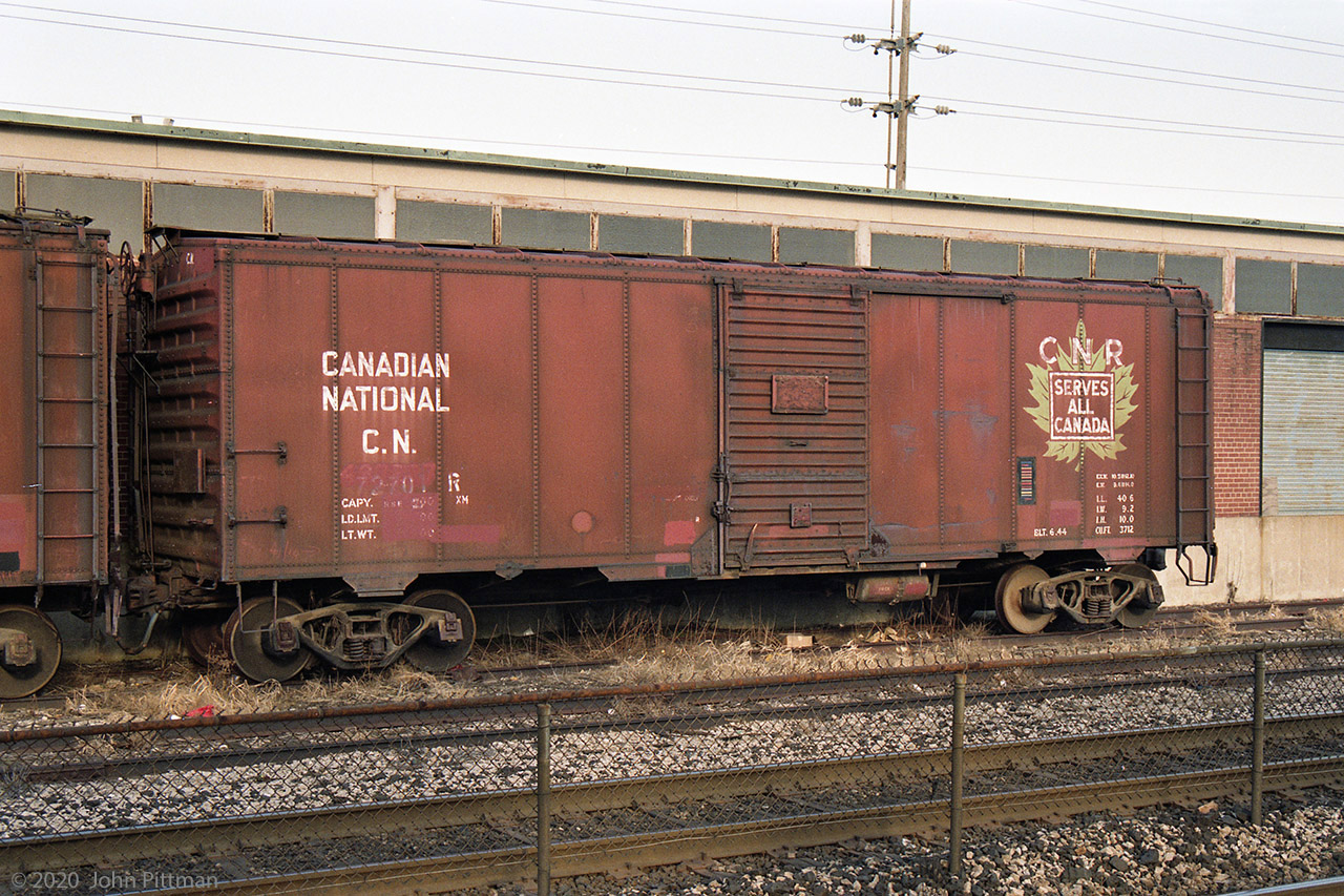 Forty foot steel boxcars were once a very common type of railcar, moving an extremely wide range of goods.
But it's quite a while since I last saw a WW2 era boxcar in Maple Leaf CNR Serves All Canada scheme.
Several of these veterans were in Oakville in 1993, retaining roofwalks, high brake wheels, "friction" plain wheel bearings, and wearing CN-service car numbers - suffixed "R" for restricted (not for interchange).
This example CN 72701R was built in June 1944, and continued in revenue service into the KarTrak colour barcode era (1967-1977). The former car number is over-painted, though some of the digits can be made out. I determined it used to be CN 467227 by magnifying and interpreting the barcode.
One of the coil springs below the faded car number has been replaced by something different.
There appears to be a triangular hole just to the lower right of the car loading door.
The car to the left was formerly CN 473453, built in May 1937.
For months (perhaps years) this pair was parked to the west of Oakville VIA Station, alongside this building marked CN Signals and Communications.
As of 2020 these cars are long gone, the north-side siding tracks are gone, and the building has gone. 
In their place is a third mainline track, and the north Oakville platform extends past here for 12-coach GO trains.