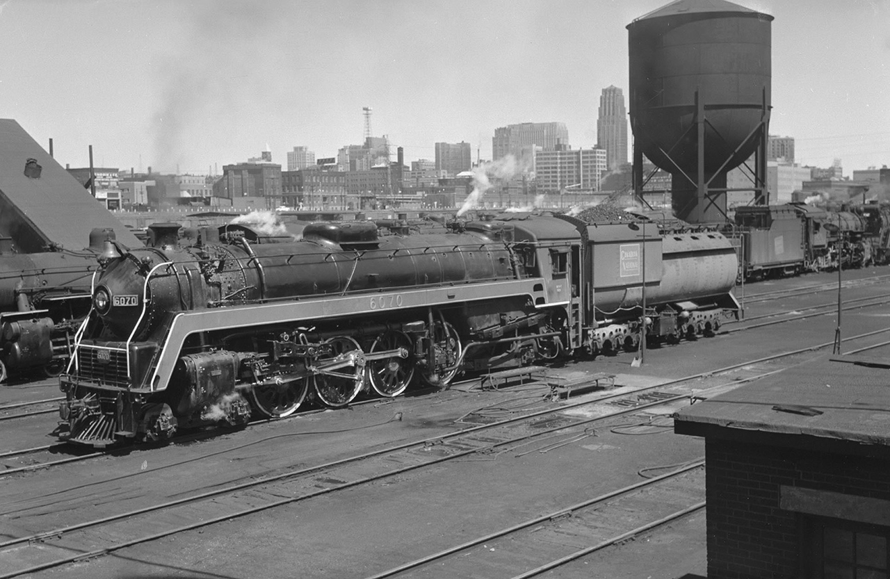 "Bullet Nose Betty" 4-8-2 CN 6070 is resting over the ashpit near Spadina Roundhouse in Toronto in 1955.
CN had 20 class U-1-F engines 6060-6079 built by MLW in 1944, retired by CN 1959-61. Three survive.
The tender is full of coal, likely filled at the coal tower on the other (west) side of Spadina Road Bridge.
Until 1962 the tallest building in the British Commonwealth was the Canadian Bank of Commerce tower (completed 1931), visible just left of CN's water tank.
James Victor Salmon photo, Courtesy of Toronto Public Library. Caption by John Pittman
