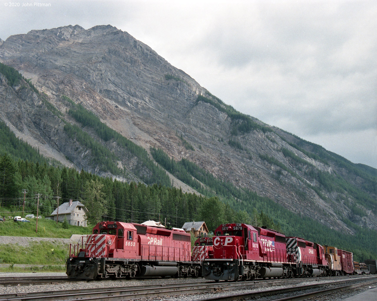 Two CP trains are waiting in Field Yard for the track ahead to clear so they can continue east.
The steep grades of the Big Hill lie ahead of them, eased to a manageable 2+ % by the spiral tunnels.
In 1993 CP mainline freight trains were predominantly powered by SD40-2's; their first GE's would arrive in 1995.
CP 5878 wears then-new CP Rail System two-flags scheme, while its trailing unit CP 6069 is in action red with the multimark. CP 6069's windows were painted red, a B-unit not intended for occupancy. First car is Angus caboose CP 434374. 
The other train is lead by CP 5653 in faded action red (no multimark), second unit CP 5870 looks similar.
Mount Stephen is nearby, but I think this south-facing view has Mount Dennis in the background.