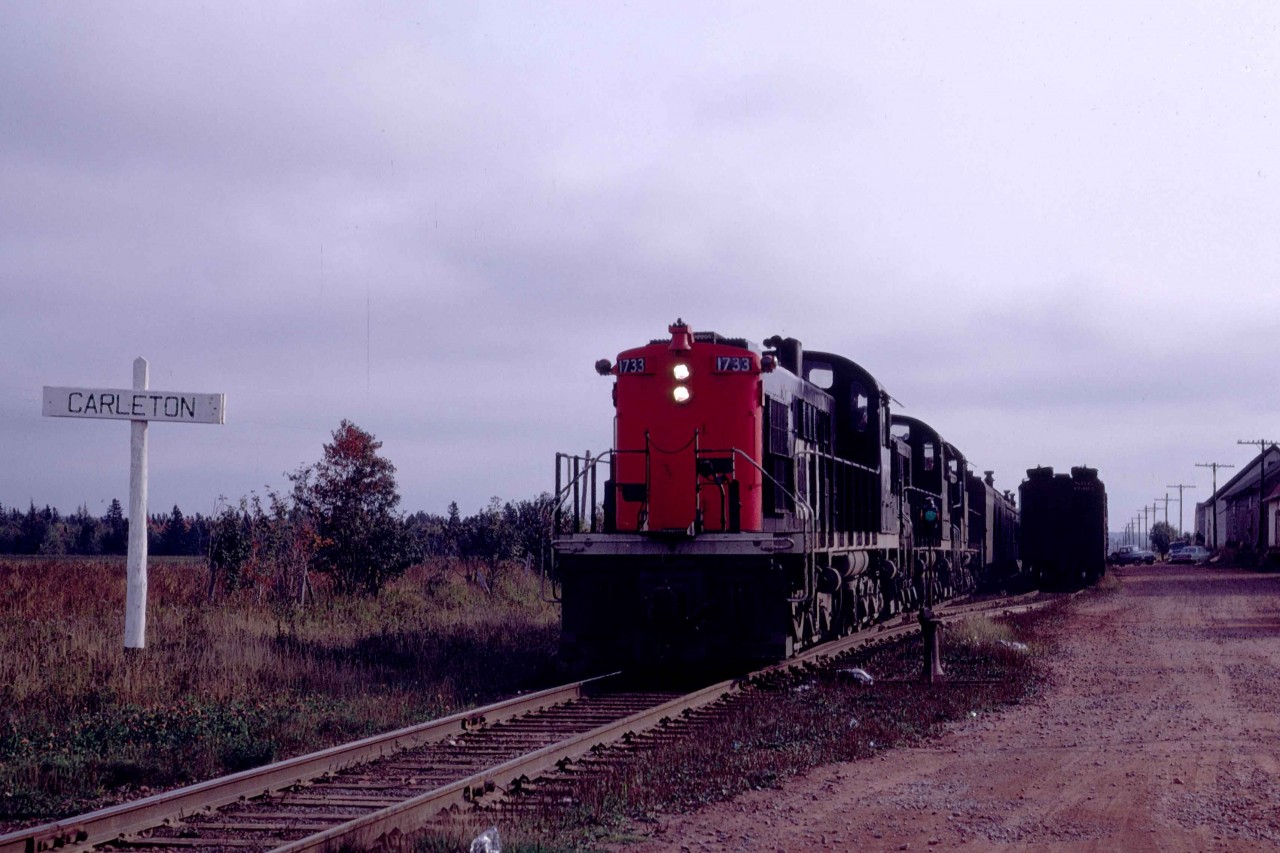 Passing Carleton, Mileage 40.9 of the Borden Subdivision, CN's Train 115 was just eight minutes away from the ferry dock at Borden, Prince Edward Island, on Saturday, October 12, 1968.  No one had set the flag, so the trio of RSC-13s motored by with a baggage car and combine at 912 a.m.  The abbreviated train had left Charlottetown, the provincial capital, at 730 for the 42.4-mile run.  I had chased the same train in May of 1968, and it had then included a full coach, rpo and three express baggage cars as well as a steam generator.   In both cases, the cars were transferred to the S.S. Prince Edward Island and off-loaded at Cape Tormentine, on the New Brunswick shore.  From there, the train continued its 6-hour run to Moncton.   I had wanted a shot at Carleton as I had graduated from the similarly named university in Ottawa in May 1967.  

Leading RSC-13 1733 was one of 35 similar MR10 units on CN.  They had arrived from MLW beginning in mid-1955 as a uniquely Canadian unit.  Their A1A trucks made them suitable for CN's many branchlines.  Tested from coast to coast, they settled in Southwestern Ontario until the mid-1960s.  With CN's determination to retire their 1200hp CLC roadswitchers, the MR10s found new life in the Maritime Provinces.  Several came to Prince Edward Island and promptly bumped a pair of H12-44s from the mainline passenger trains and 70 Ton GE's from many secondary routes, excluding those south of Mount Stewart, east of Charlottetown.   By the mid-1970s, their 6-cylinder McIntosh and Seymour inline 1,000hp engines were out of favor on CN.  So, they were retired, and their trucks placed under de-rated and lightened RS-18s in a program conducted by the Moncton Shops.  For example, 1733 was retired on Wednesday, October 8, 1975, and its trucks installed under RS-18 3845, which became RSC-18 1752 when it re-entered service on Friday, October 24, 1975.   CN assigned 1750 through 1756 to Charlottetown in 1979.   On Wednesday, August 25, 1993, CN sold the unit for scrap to Met-Recy in Laval, Quebec.  It was resold to the Deleware-Lackawanna but was subsequently rejected and presumed scrapped.