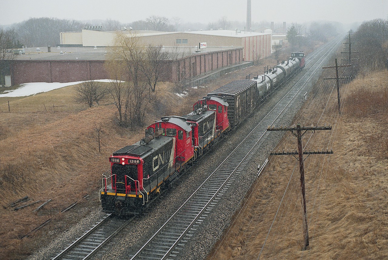 As usual, I seem to be out more on crappy days than good ones, and I see this is no exception. But it was a day off work and you have to take what you can get.
It is late March and I preferred the flurries coming down rather than rain.
CN 1388 and 1355 are seen here upon their return from Hamilton. I think this is train #555, but not sure, as I did not mark the photo.  I do miss these old SW switchers; they seemed so reliable and practical from a fans' point of view. Once, they seemed to be everywhere.
In this image, the tall stack in the background is the site of the former Burlington Brick plant. The area is all homes now; brick plant is history.