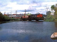CN RS18 3708 works local freight #590 along the former Thousand Islands Railway line (now known as CN's Gananoque Spur), crossing the Gananoque River between River Street and King Street. The spur line branched off near Cheeseborough at Mile 155.3 of CN Kingston Sub and extended 3.2 miles south into the Town of Gananoque, following the Gananoque River. Interestingly, the line diverged about a mile west of the CN Gananoque station location, once known as "Gananoque Junction".<br><br>The Thousand Islands Railway was originally constructed in the 1880's as a way to connect port and lumber facilities in the Village of Gananoque to the Grand Trunk Railway's mainline, and in 1911 GTR took control of the TIR. The name of the line was retained until 1958, and CN continued to operate the line as a spur until dwindling traffic warranted abandonment in 1996, and removal in 1997 (parts of the right of way are now the Gananoque Waterfront Trail).<br><br><i>Keith Hansen photo, Dan Dell'Unto collection (with some colour correction and restoration work done).</i><br><br><i>For more history on the line, refer to Ray Kennedy's Old Time Trains page <a href=http://www.trainweb.org/oldtimetrains/CNR/TIR.htm><b>here</b></i>.