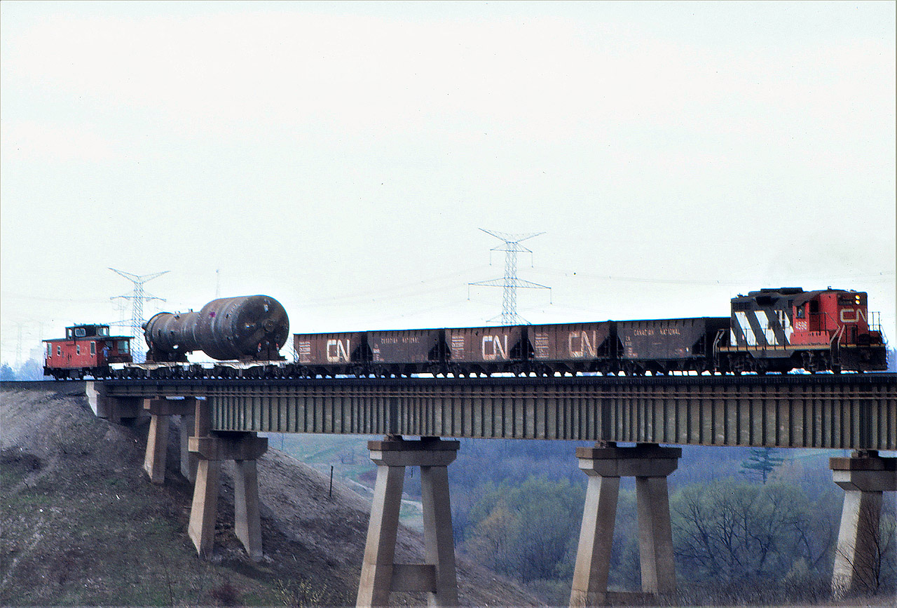 A CN special train with GP9 4596 creeps over the single track Humber River bridge on CN's Halton Sub with a huge load for Ontario Hydro's Darlington Nuclear Power plant which was under construction at the time.  The hoppers were each loaded with about 40 tons of sand for extra braking power.