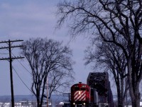  The Nackawic Turn is close to its home terminal in Fredericton, New Brunswick, on a beautiful afternoon in March 1985.  It is about to pass the site of the former CNR Fredericton station on the engineer's side of the tracks.<br><br>C-424 4218 was built in Montreal, Quebec, by MLW and delivered as the 8318 on Tuesday, October 5, 1965, with serial 84856.  The CPR received trade-in credit with the return of Alco FB-1 4402 on Thursday, July 8.  The unit was part of 32 unit order 4905, class DRF-24b, built between March and December 1965.  Their delivery was followed immediately by order 4906 for 18 units of class DRF-24c.  MLW built these without trade-ins from December 1965 through March 1966.  CPR initially used the C-424s on priority freights, notably on the Eastern Region, as St. Luc was their original maintenance assignment.  When they were new, I often saw them on Windsor - Montreal hotshots in combination with the nearly new GP35s, which had proven slippery.  CPR quickly renumbered the units in the 4200 series.  Retirement, conversion or sale came to the C-424s before 1996; however, the 4218 was not one of the 31 survivors.  It was tied up unserviceable on Thursday, March 23, 1995, retired on April Fools Day and sold to MetRecy in Laval, Quebec for $8,750 on Wednesday, June 21.<br><br>The Nackawic Turn left Fredericton weekday mornings with traffic for the paper mill at Nackawic on the north side of the Saint John River.  At Una Junction, Mileage 21.8 of the Fredericton Sub, the outbound train turned north on trackage rights at Mileage 0.2 of the CNR Fredericton Spur and joined their 70.5-mile Saint John - South Devon Oromocto Sub at Mileage 69.4.  The Turn then crossed the bridge in the background.  (On Monday, March 16, 1936, the ice blocked river destroyed the original crossing; this bridge opened on Wednesday, June 1, 1938.  It survives as a walking path.)   Reaching South Devon on the northern bank, the train turned north for a 37-mile run to Southampton on the Gibson Sub.  At Southampton, Mileage 22, it turned south, travelling 9.4 miles to the mill at Nackawic.<br><br>Upon returning to Fredericton, the power was set up to do a nightly 133.2-mile turn to Saint John.  This arrangement ended on Friday, October 25, 1985, thereafter power from mainline freights brought cars the 22.2 miles into town from Fredericton Junction on the Montreal - Saint John line.   Prior to Friday, November 28, 1980, the nightly freight, the "Oriental', took its train to McAdam, forty miles west of the Junction.<br><br>The 1967 flooding behind the Mactaquac Dam caused the relocation of several communities. It spawned the province's first model community in Nackawic.  The flooding also cut short the last 3.1 miles of the Southampton Sub that reached down to the Saint John River at Otis.  St. Anne Nackawic Pulp and Paper opened their kraft pulping mill in 1970 and received a continuing supply of rail-hauled Bunker 'C' oil from the Irving refinery in Saint John.   Rail shipments lasted until Monday, November 29, 1993.  At the end of 1994, CP Rail discontinued its operations east of St. Jean, Quebec and abandoned its branchlines north of Fredericton.   The present owner, AV Group NB Inc., produces up to 540 metric tons of bleach kraft pulp daily.