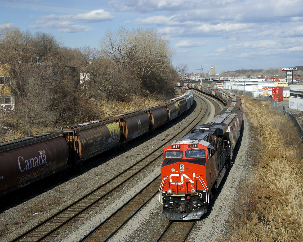Shiney CN 3887 brings up the rear of grain train CN 874, which is leaving Turcot Ouest after changing crews there. At left grain cars are stored on the transfer track.