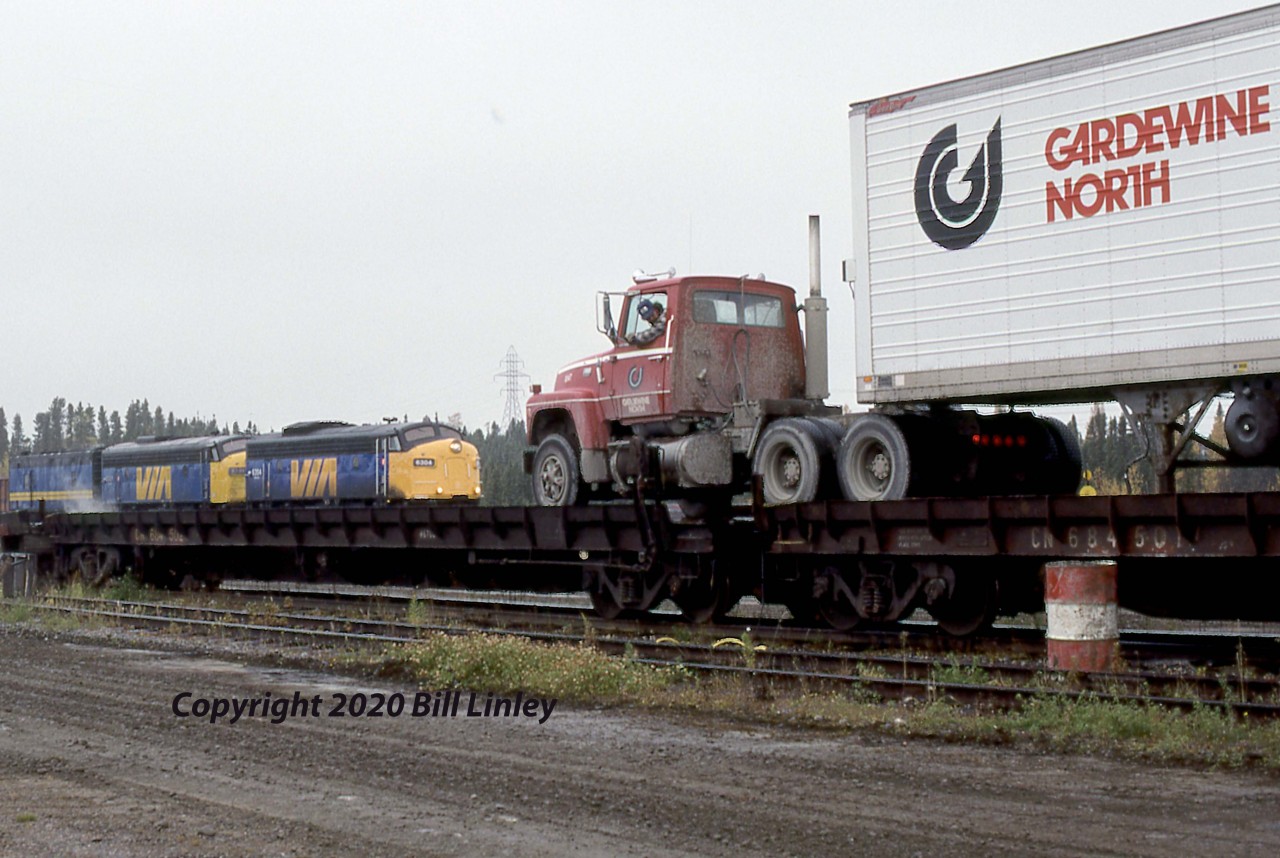 F Unit Friday

VIA FP9 6304 waits in the background while workers loaded piggyback flats at Thompson, Manitoba, in October 1991.  Train 93, the tri-weekly Hudson Bay from Winnipeg, some 700 miles to the southeast, would lift three flats during its 90-minute supper-time layover in Thompson.  The Ford tractor is loading the first of three Gardewine trailers that VIA will deliver to Churchill some 347 miles and 13 hours away.  The railway is the only year-round access to the Hudson Bay port of Churchill.   

VIA 6304 began life as CN 6509 (GPA-17a, GMDL 1956 #A639).  Via had the unit rebuilt at CN's Pointe St-Charles shops in Montreal in 1984 with a 16-645 prime mover, classed as a GPA-418a.  It was the last of five similar units that had their steam generators removed for service on the Churchill line.  In 1967 it was renumbered 1967 and was the trailing unit to CPR FP9A 1411 on Canada's Centennial Train.  As VIA retired its steam-heated cars, it received a 275kW head-end power unit in 1997 and was subsequently withdrawn in 2002 and sold to IFE Leasing of Saugus, California.  Edmonton, Alberta, is presently the storage site for VIA 6304.

The year 1910 marked the first planning for a railway to Churchill, and initial construction was begun in 1912 by the Canadian Northern.  Bankruptcy intervened, and the CNR finally completed by the line in 1929.  CN sold the route to Colorado-based OmniTRAX in 1997.  Operation of their Hudson Bay Railway line continued until major washouts in 2017.  Some two years later, operations resumed under new ownership: Fairfax Financial Holdings & AGT Limited Partnership and Missinippi Rail Limited Partnership, representing First Nations members and residents.  

Gardewine is a multi-purpose transportation company headquartered in Winnipeg and is now a subsidiary of the Mullen Group Ltd. of Okotoks, Alberta.