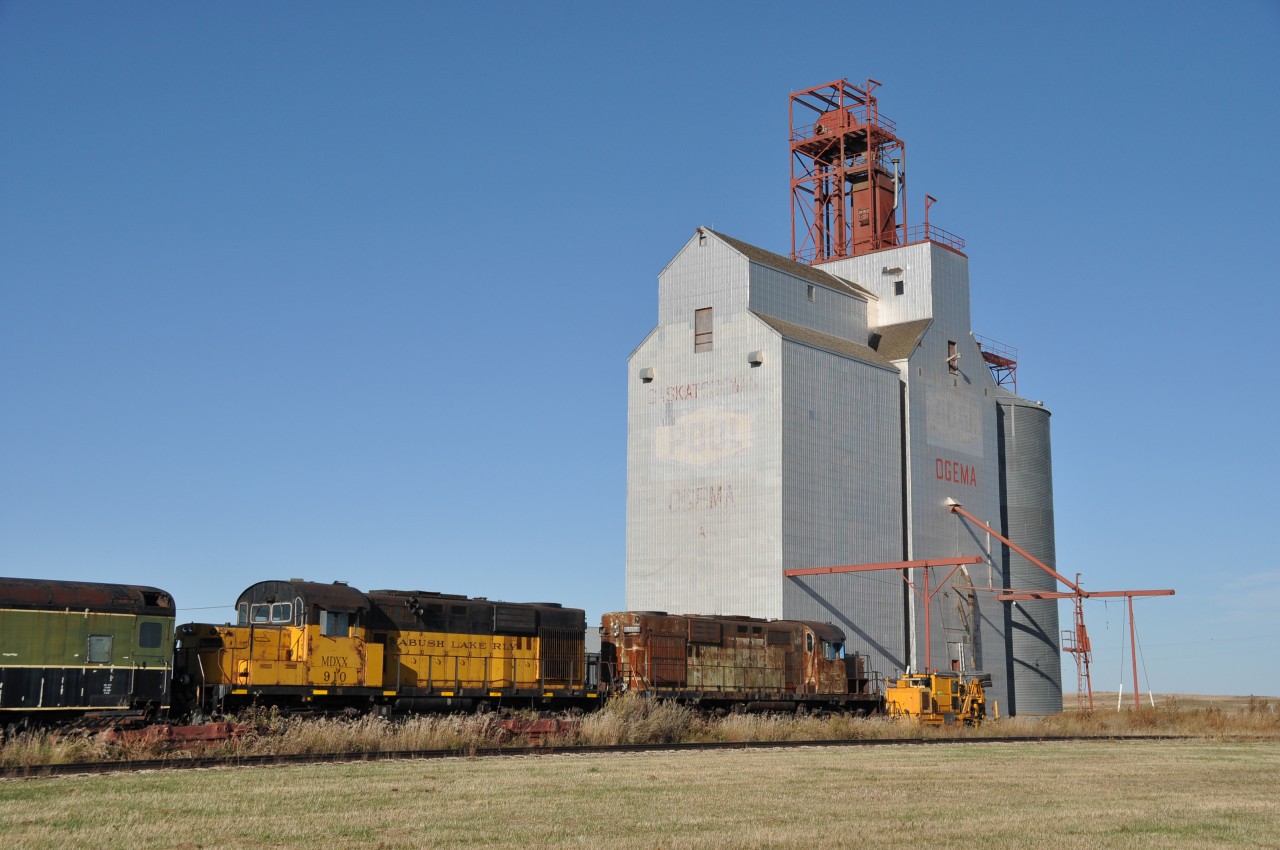 Rather sad looking old former Wabush Lake Railway locomotives are seen rusting away below the Ogema grain elevators just south-east of the community. The units now sport reporting marks MDXX and are #910 and 909.
They're on the property of, or close to, the Ogema's Southern Prairie Railway; a nifty tourist train operation in town on former CP trackage. This operation is well received and usually runs June 1 to Sept 30th annually.
No idea what is to become of these odd looking low nose RS-18s. Not much, by the look of them.